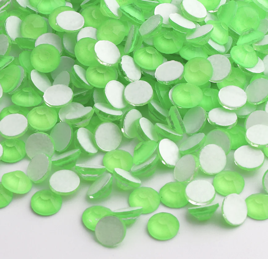 Green and white flatback rhinestones scattered on a white surface.