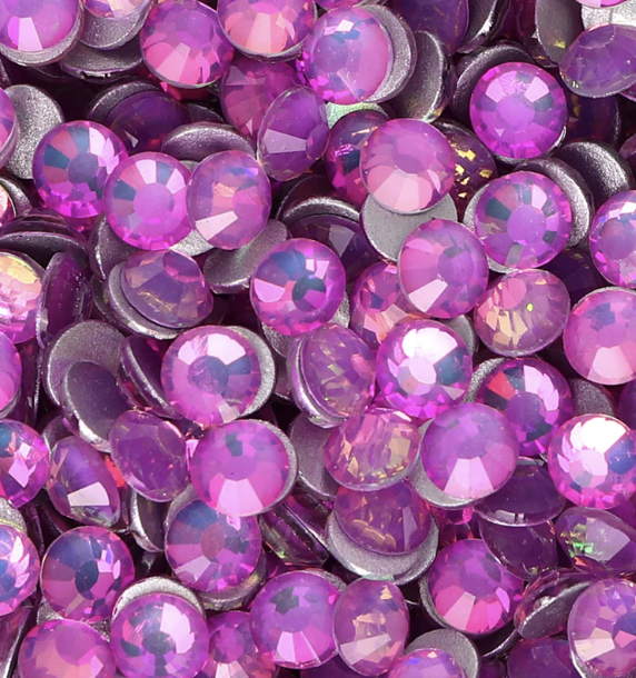 Close-up of numerous pink and purple rhinestones with faceted surfaces, some with iridescent effects, scattered in clusters.