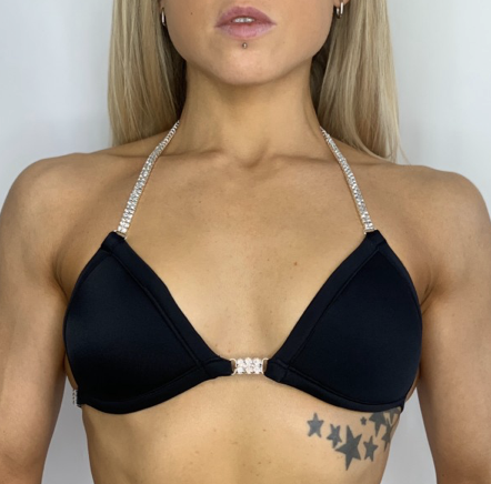 Close-up of a woman's upper body wearing a black bikini top with rhinestone straps and a star tattoo on her stomach.