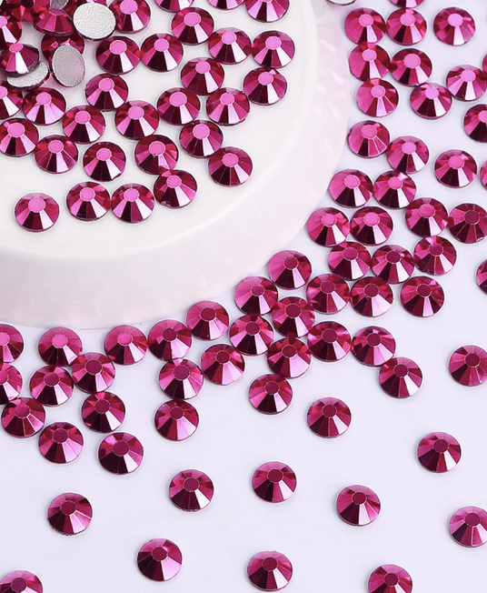 Pink rhinestones scattered on a white surface around a white circular object.