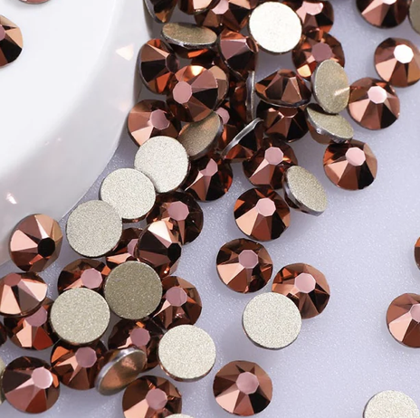 A collection of small, round, copper-colored rhinestones and flat, matte gray gems scattered on a light surface.