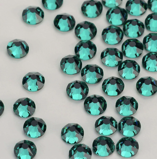 Multiple teal-colored rhinestones scattered on a white surface.