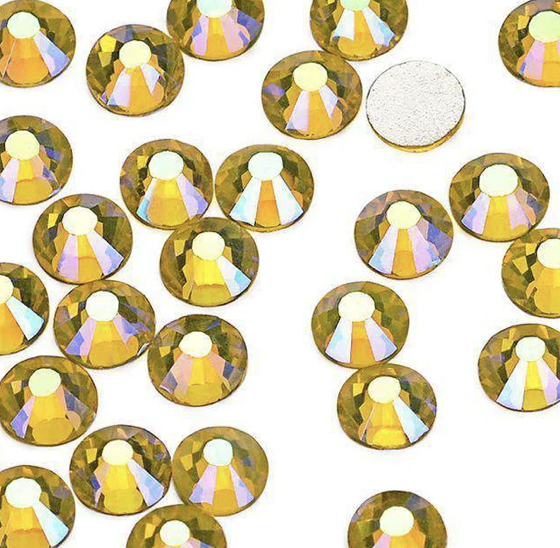 Gold and iridescent rhinestones scattered on a white surface, with one plain white rhinestone among them.