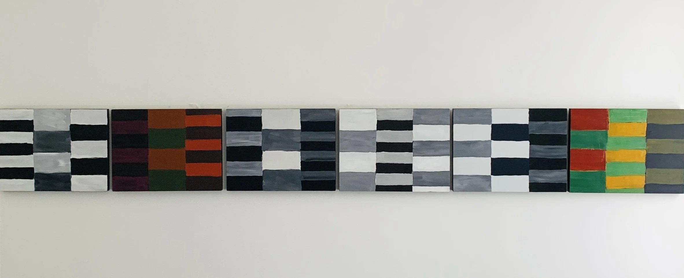 A series of small abstract paintings with varying geometric black, white, gray, red, green, yellow, and orange patterns, arranged horizontally on a white wall.