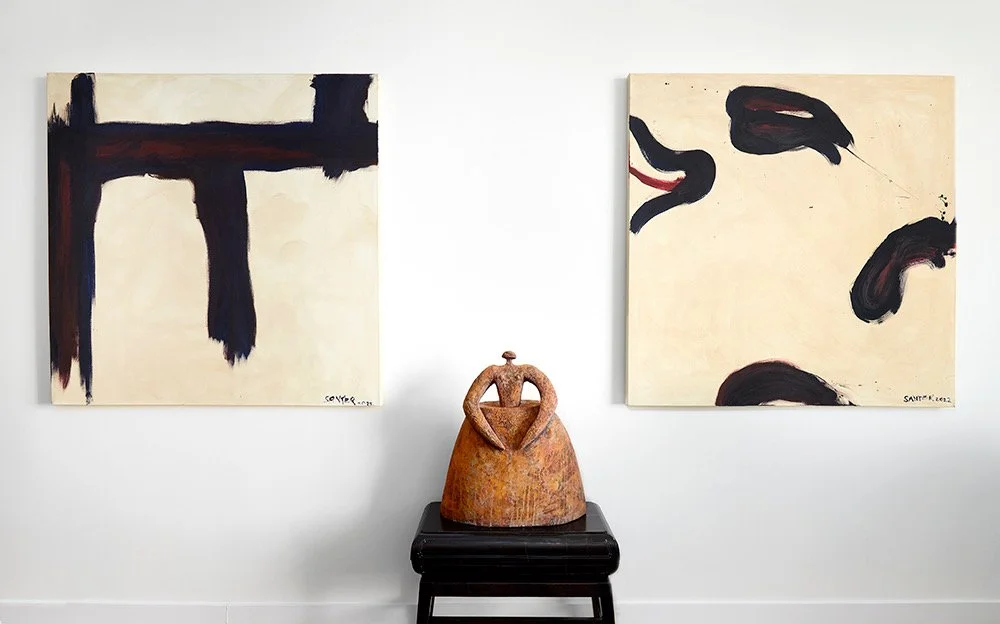 Two abstract paintings on a white wall with a ceramic sculpture on a black stand between them.