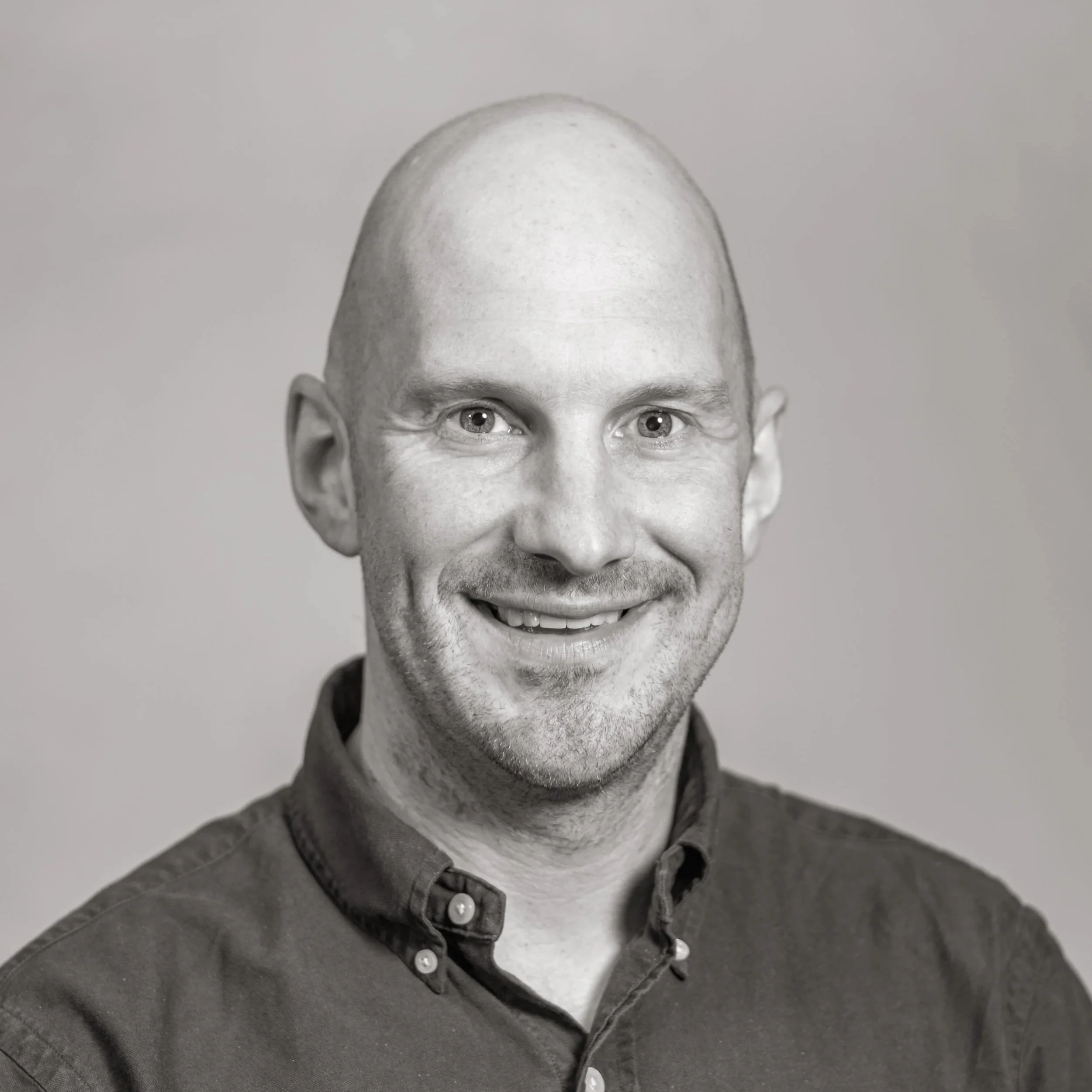Black and white headshot of a smiling man with a bald head, wearing a collared shirt.