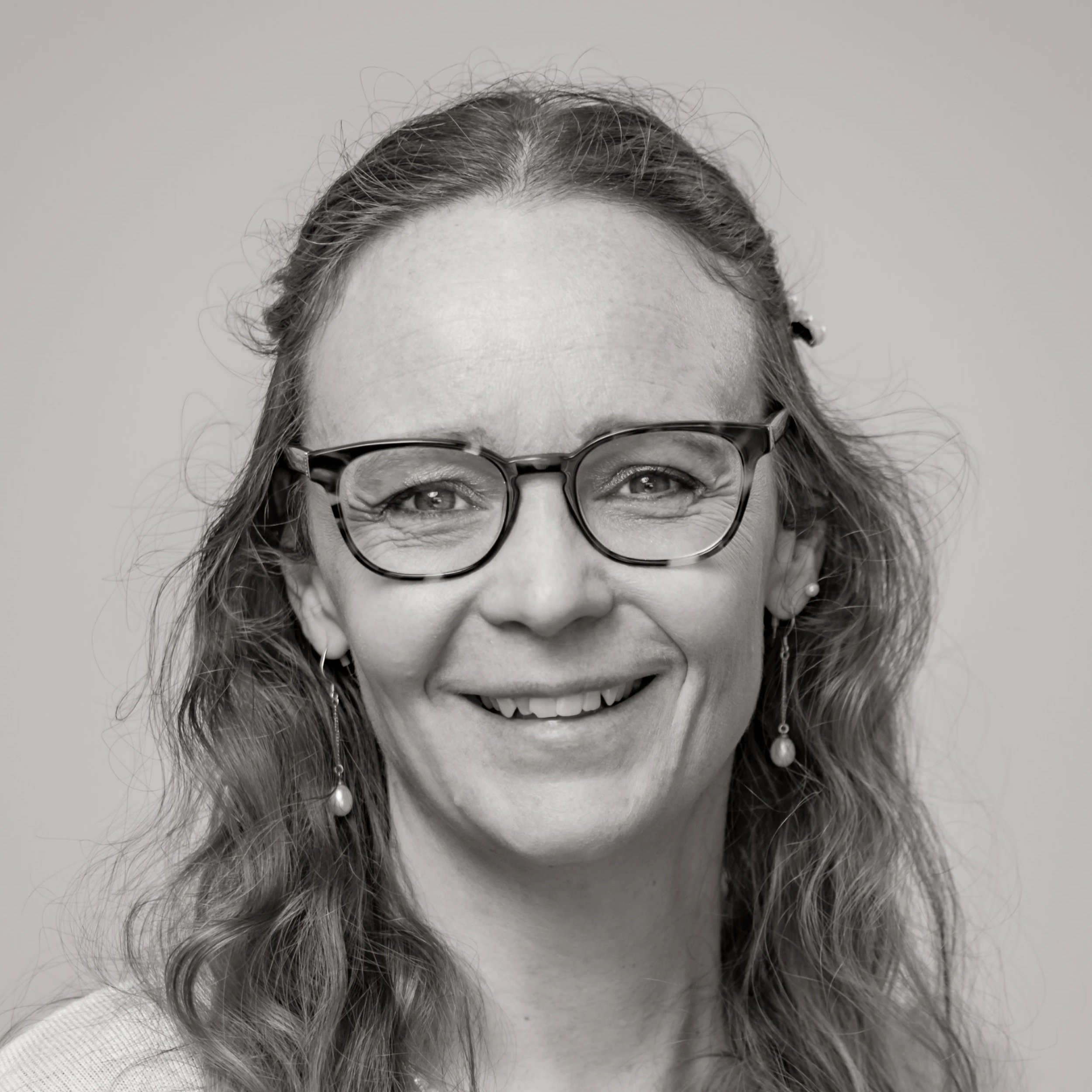 Black and white portrait of a smiling woman with wavy hair, glasses, and earrings.