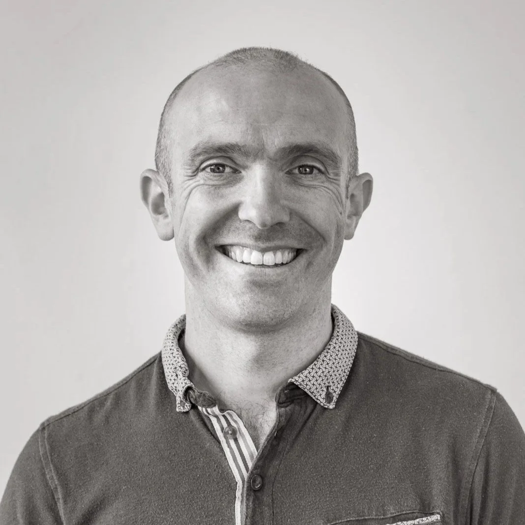 Black and white portrait of a smiling man with short hair, wearing a collared shirt and jacket.