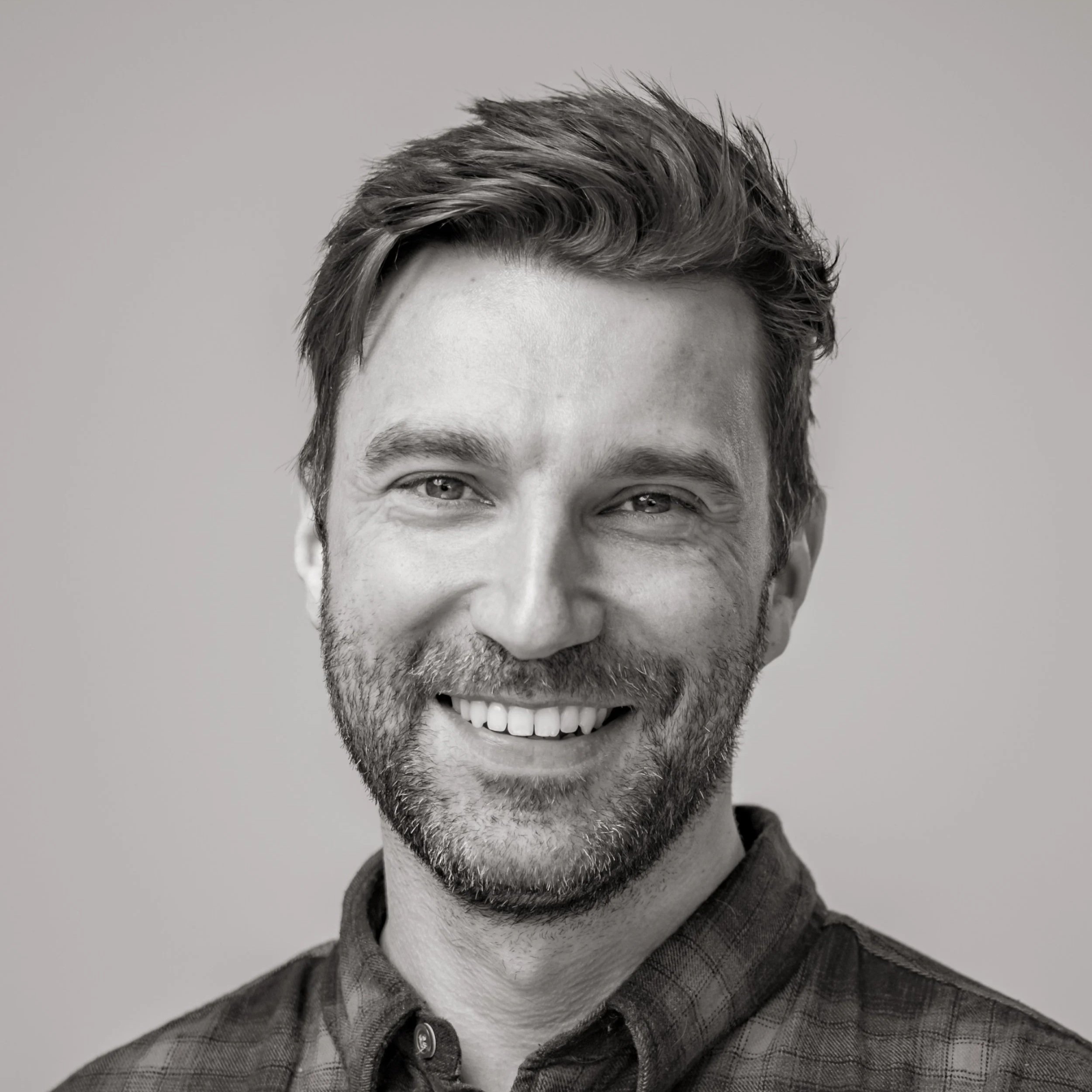 Black and white portrait of a smiling man with styled hair and a beard, wearing a button-up shirt.
