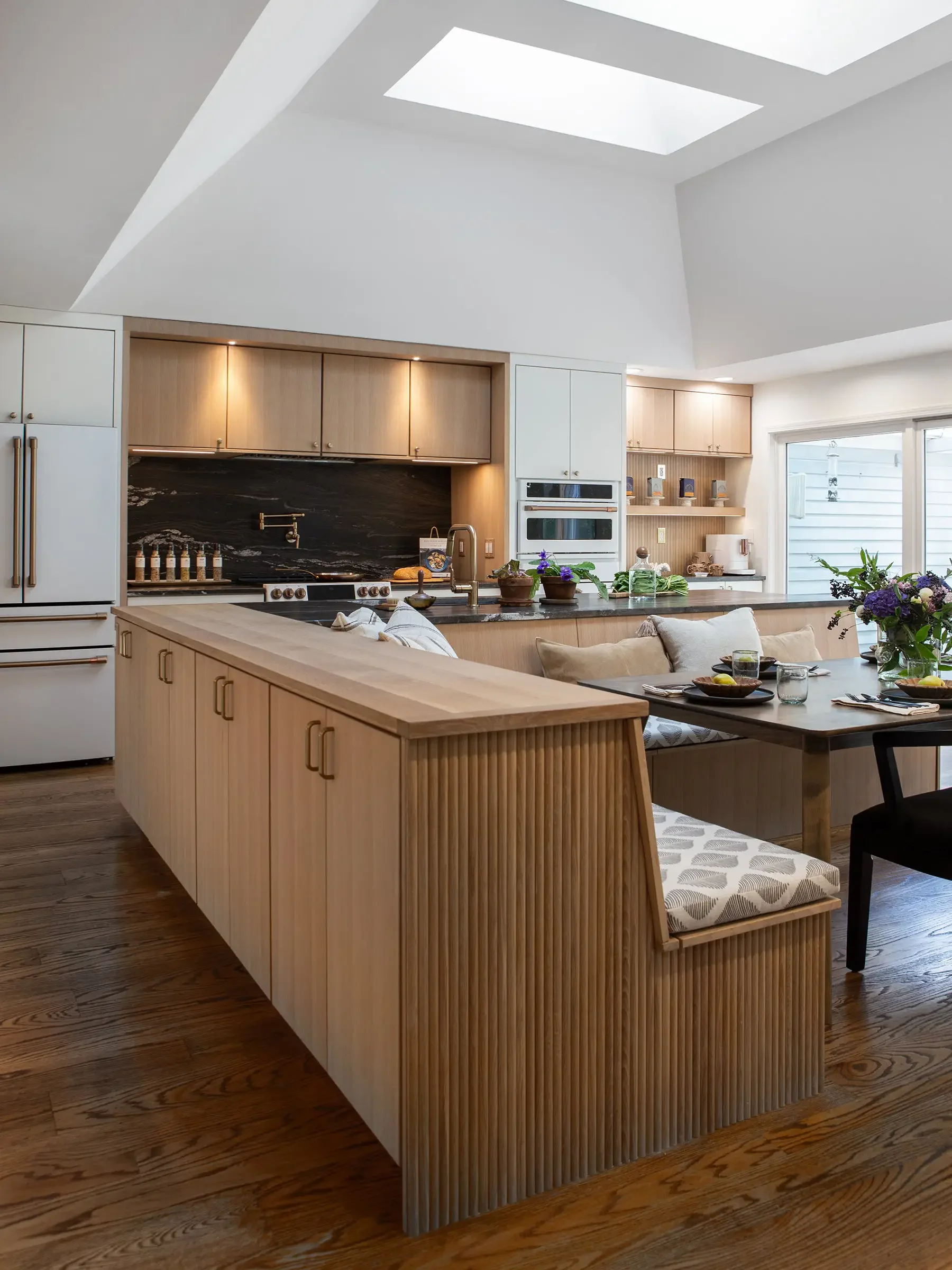 Modern kitchen with white and wood cabinets, a black stove, a window, and a dining table with a bench and chairs.
