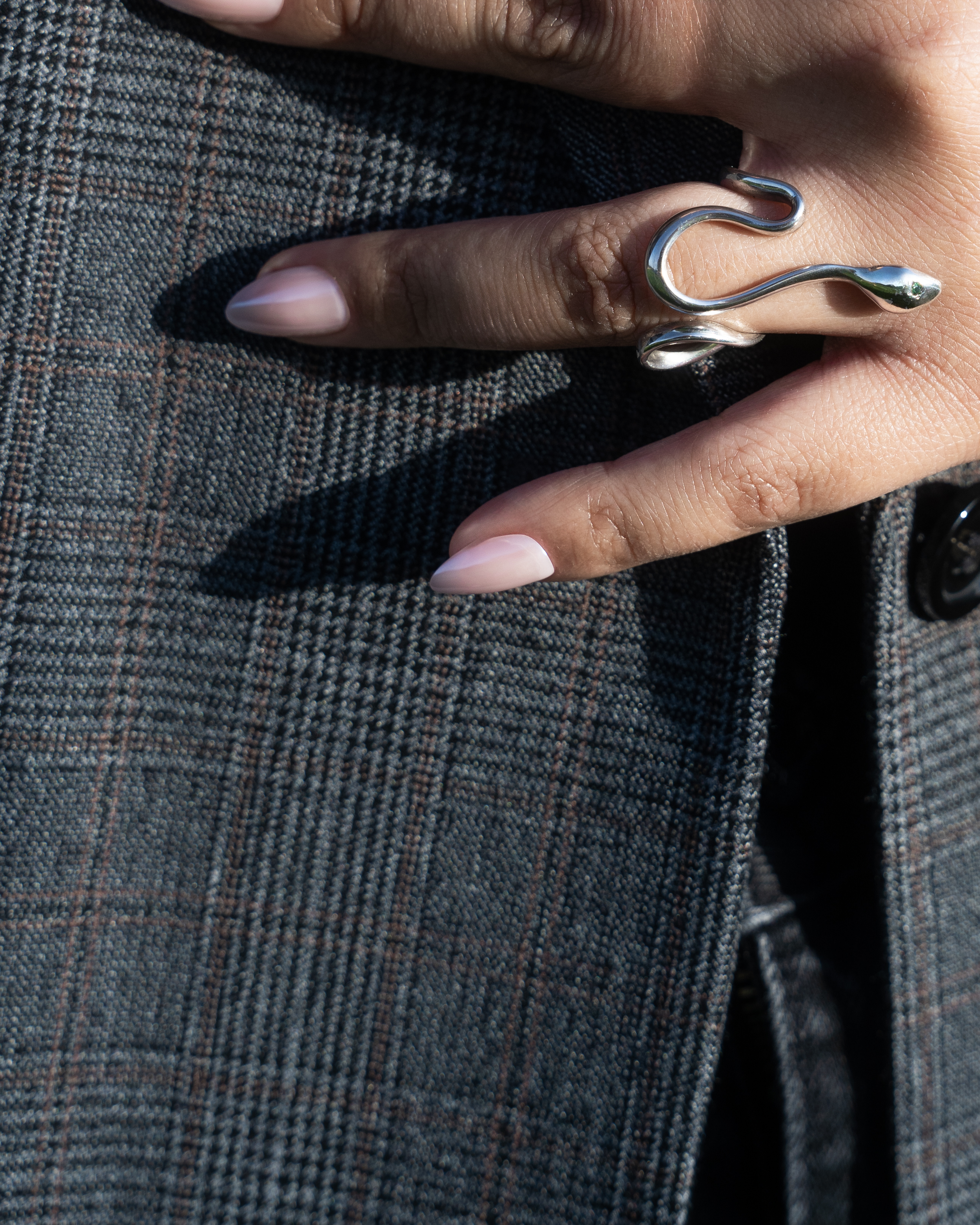 A hand with long, manicured nails wearing an elongated silver ring shaped like a snake, resting on a plaid patterned fabric.