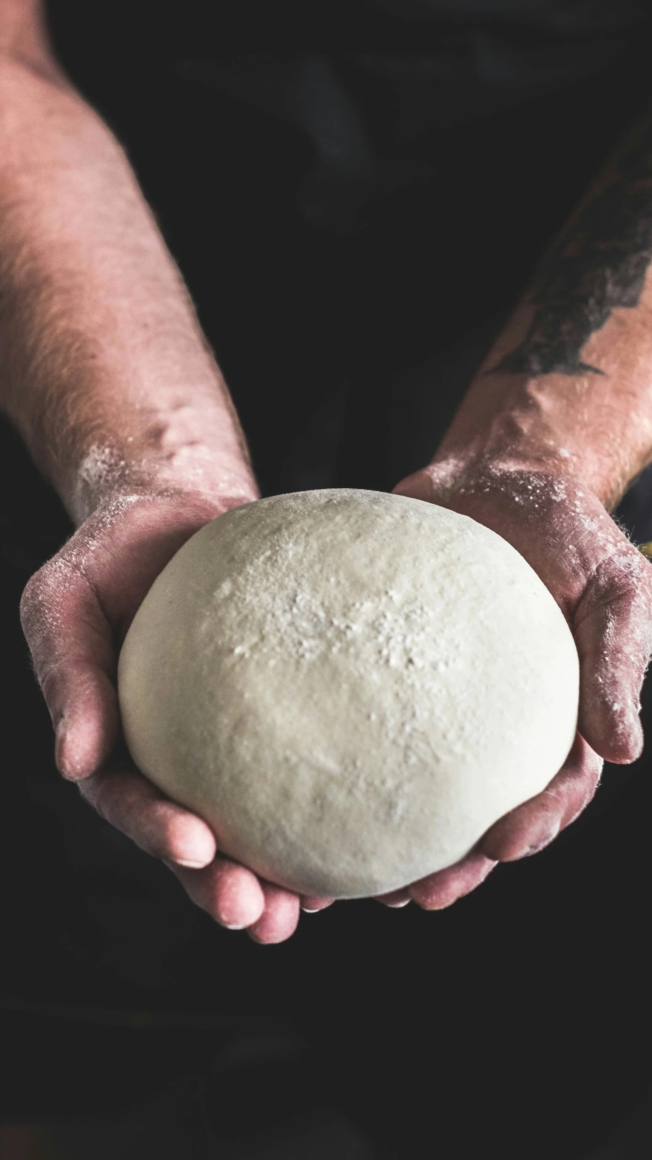 Person holding a round ball of dough dusted with flour.