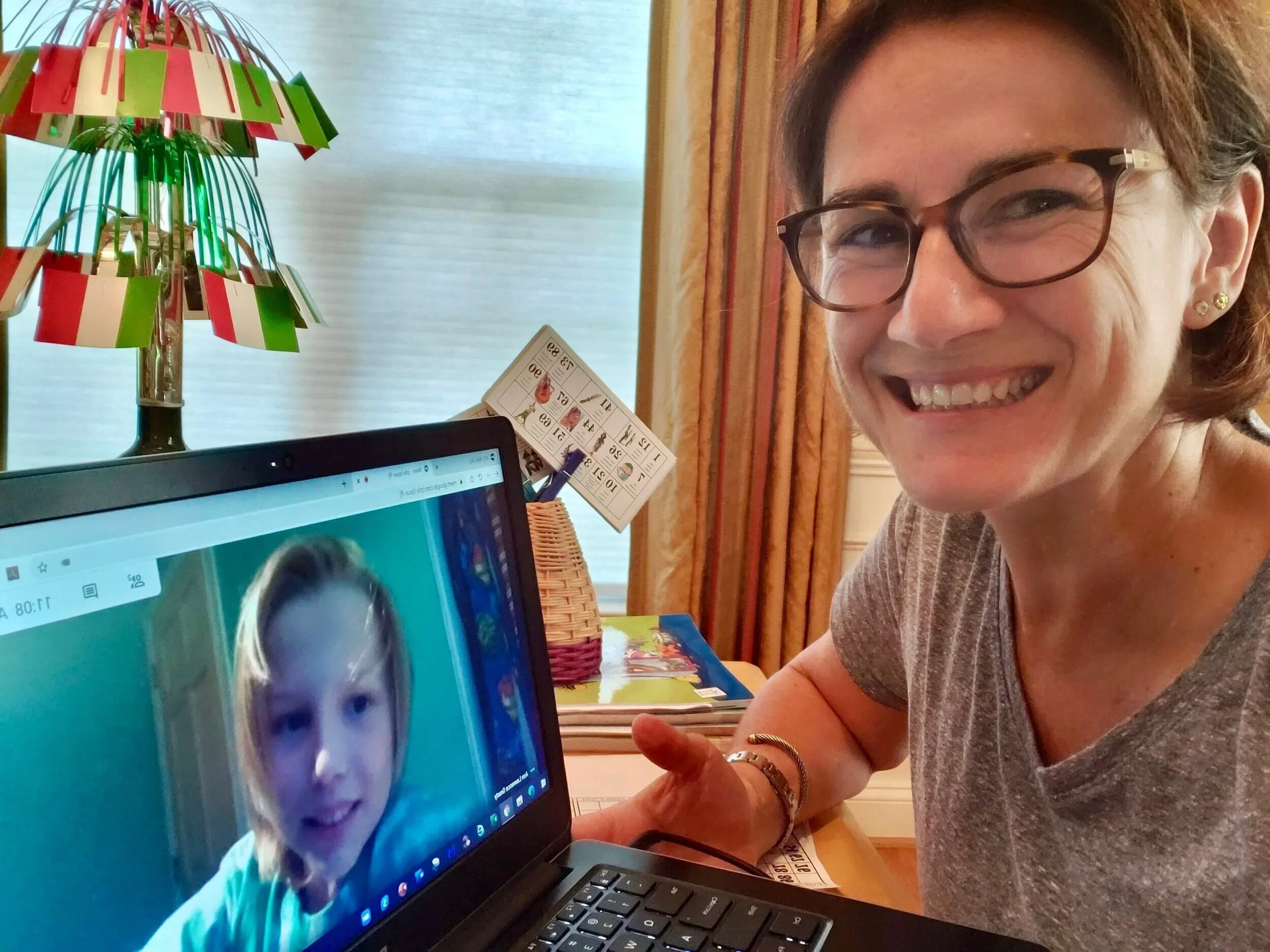A woman holding an activity card beside a laptop video call.