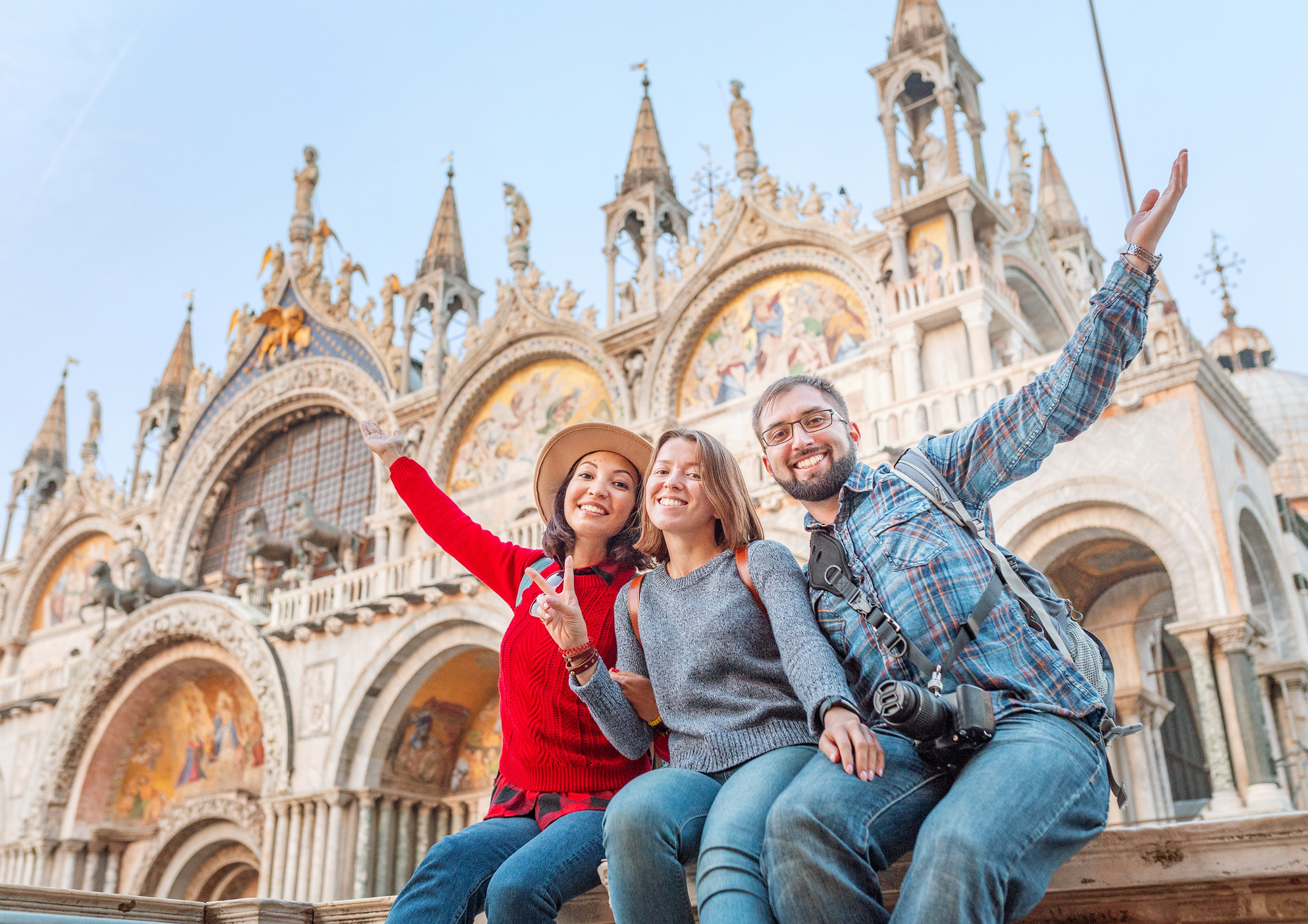 Tourists smiling and posing in front of St. Mark's Basilica in Venice, Italy.