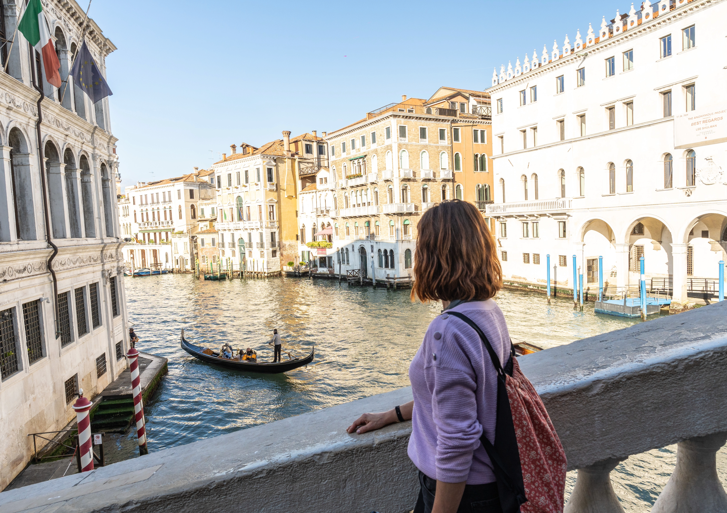 A woman looking over a canal in Venice, Italy, with boats and historic buildings in the background.