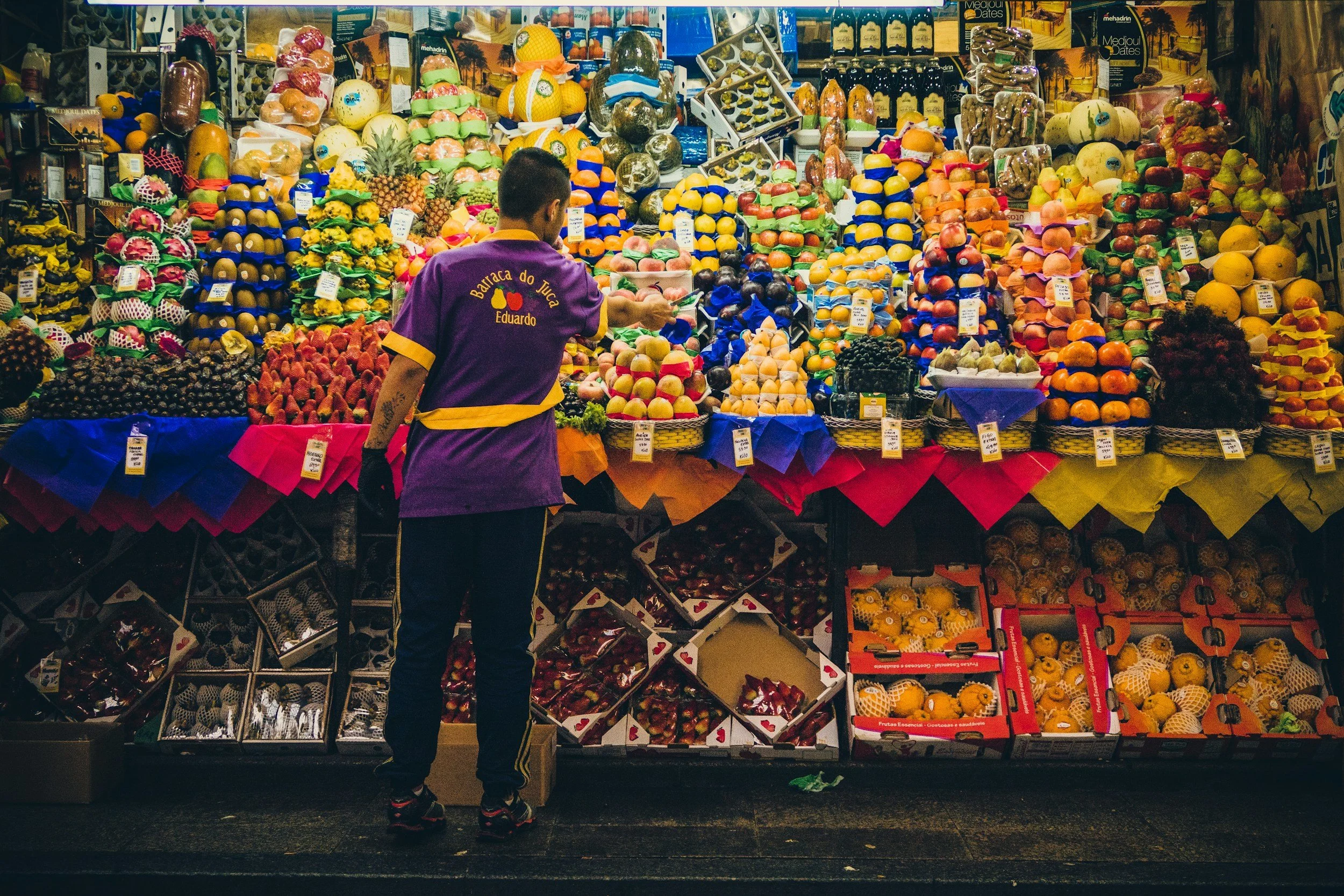 A man looking at a colorful display of various fruits at a market stall.