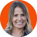 A woman with shoulder-length gray hair and a big smile, standing in front of an orange background.