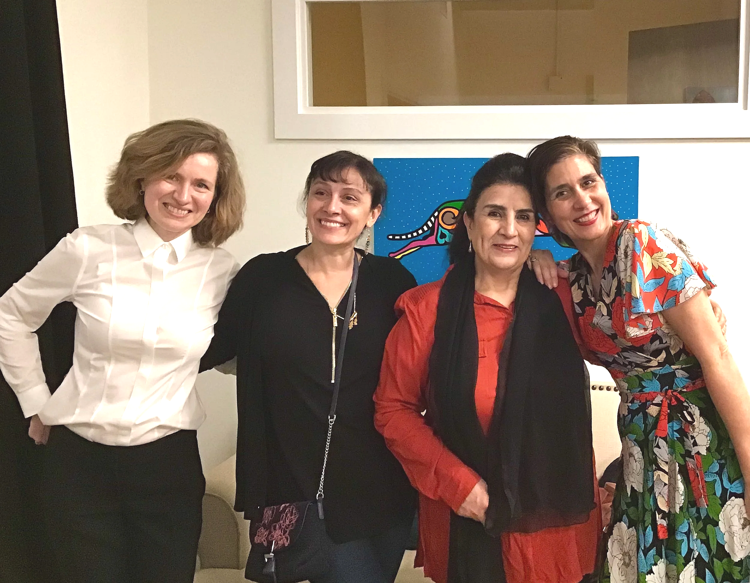 Four women smiling together indoors.