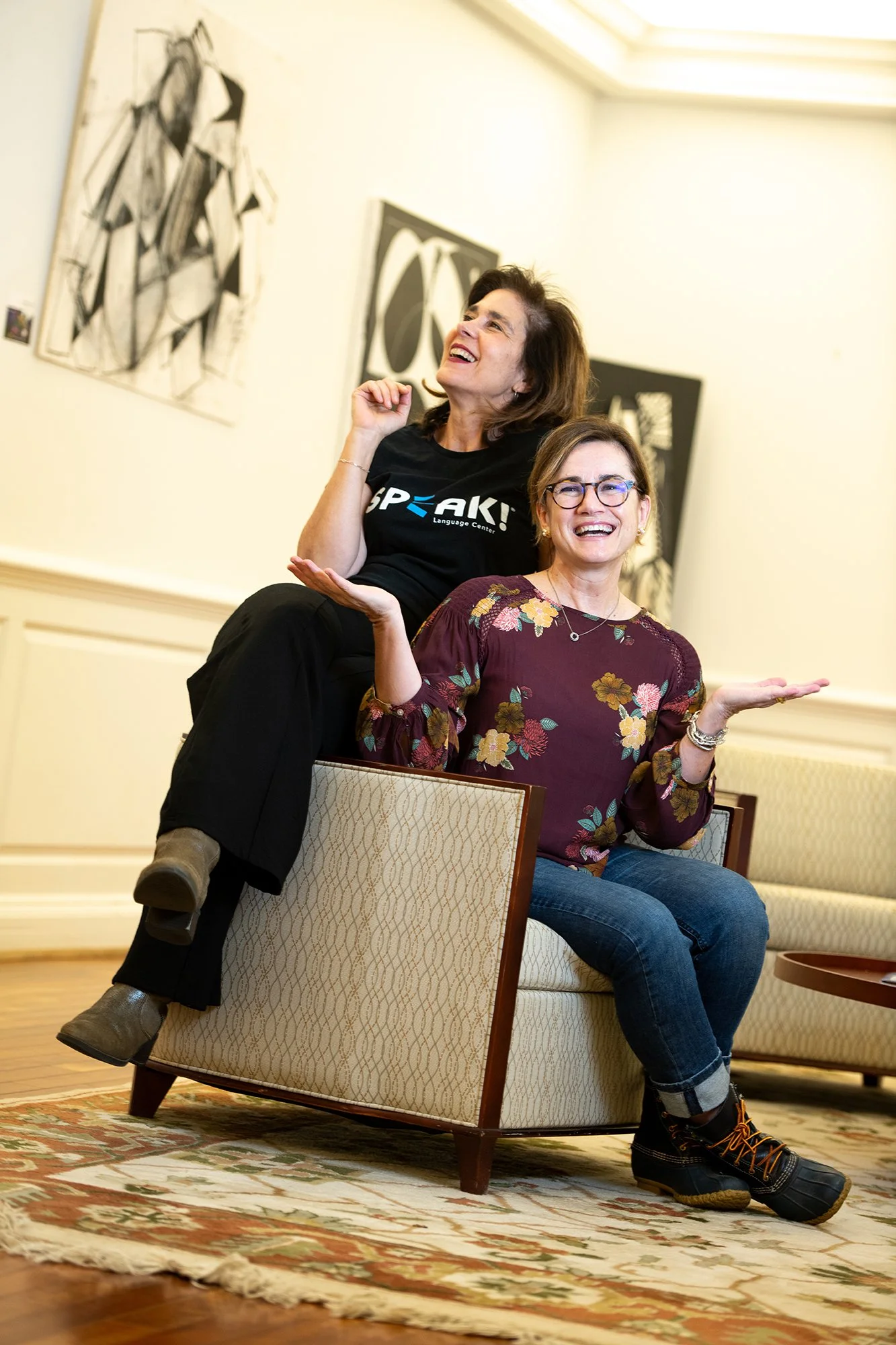 Two women laughing together beside abstract artwork.