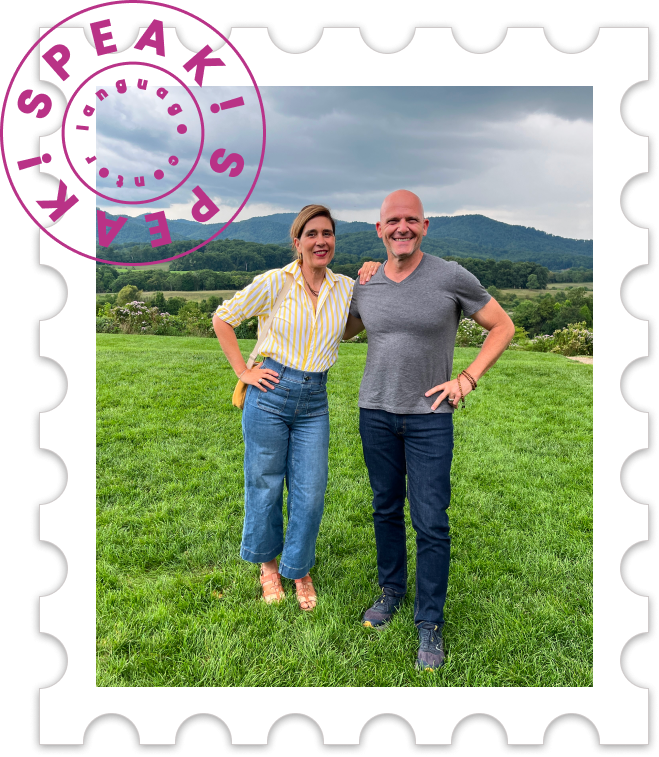 Two smiling people standing outdoors on green grass, with rolling hills and cloudy sky in the background, framed by a stylized postage stamp border with purple and black accents.
