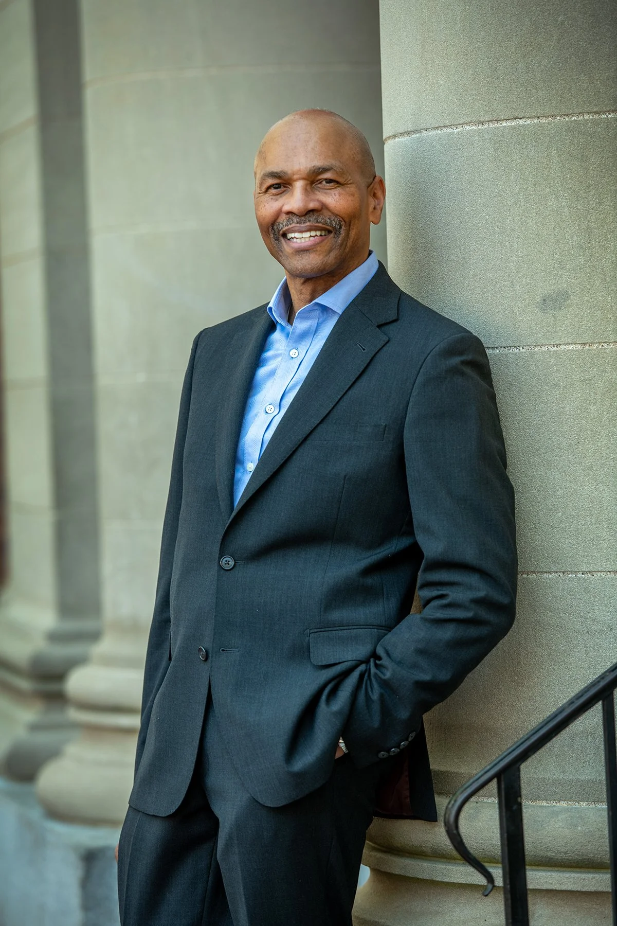A smiling man leaning against a stone column.