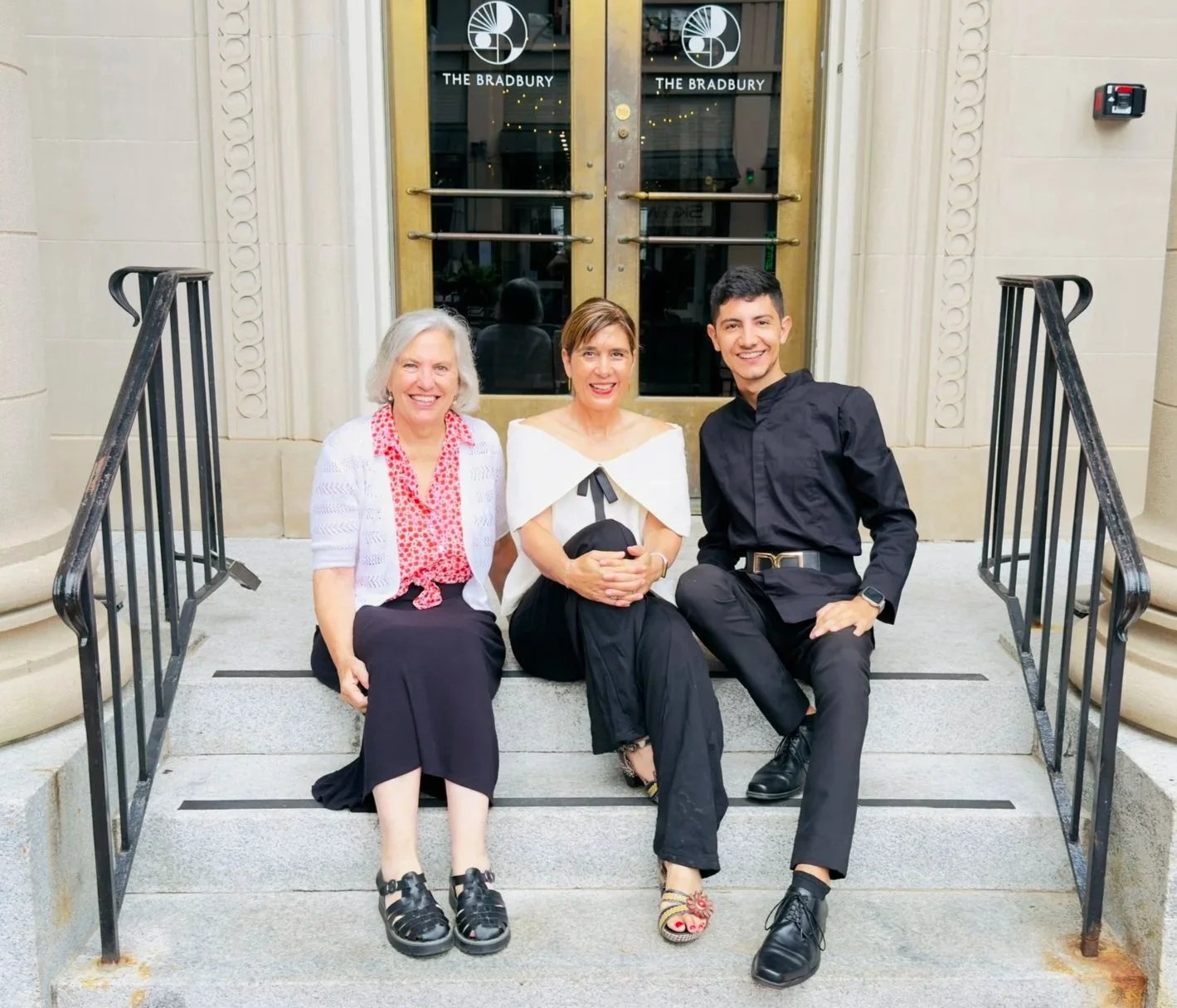 Three people smiling on the steps outside The Bradbury.