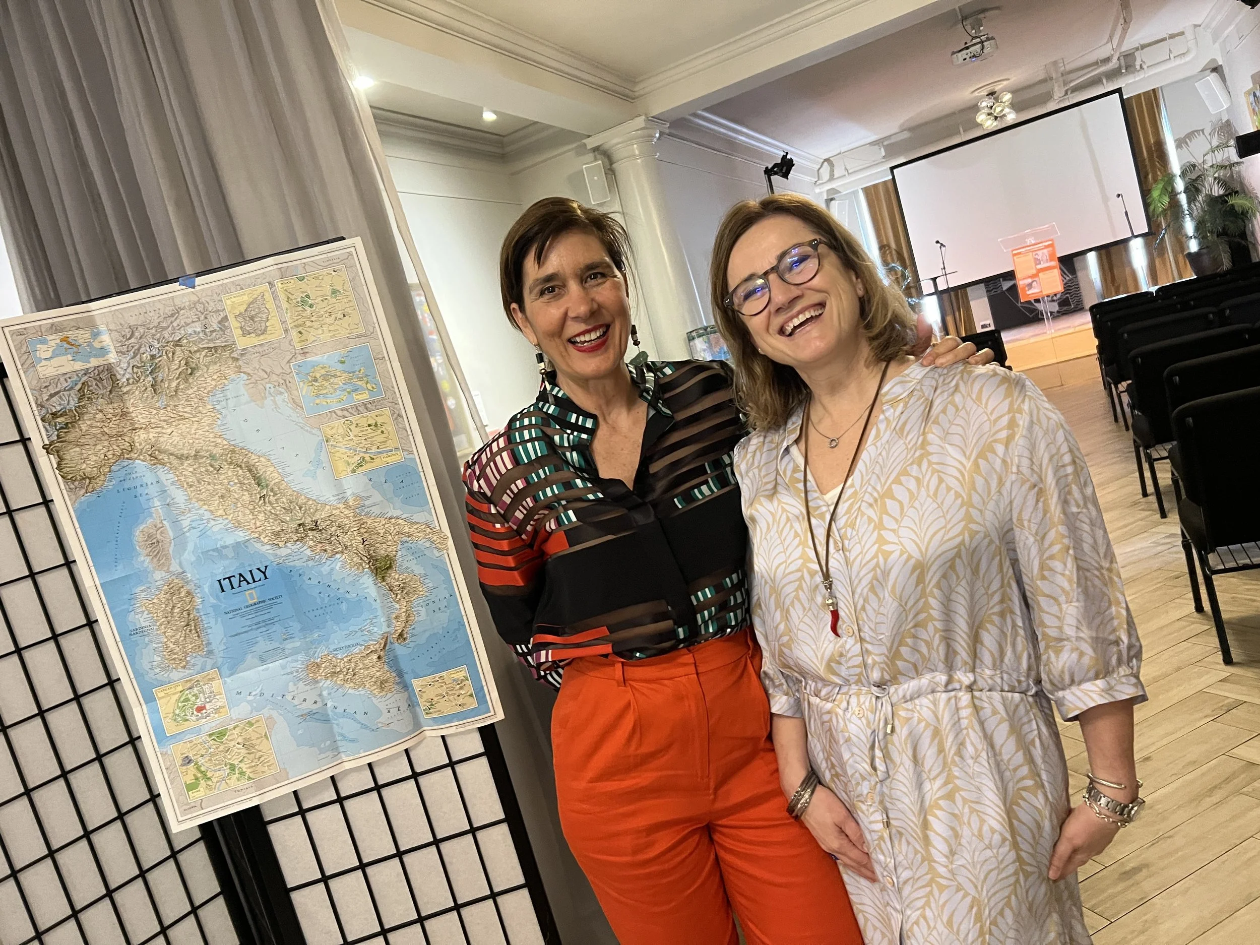 Two women taking a selfie beside a map of Italy.