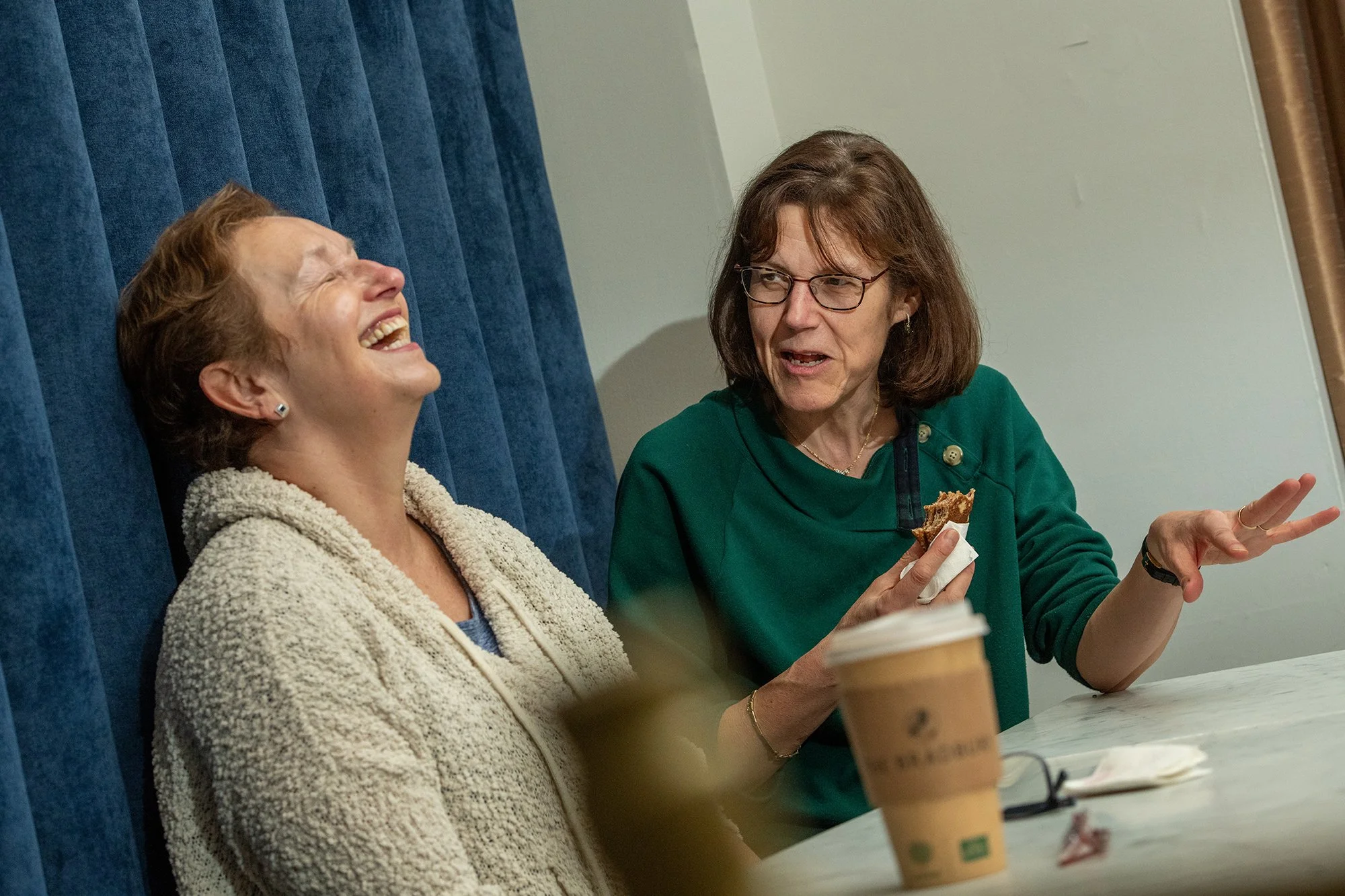 Two women talking and laughing over refreshments.