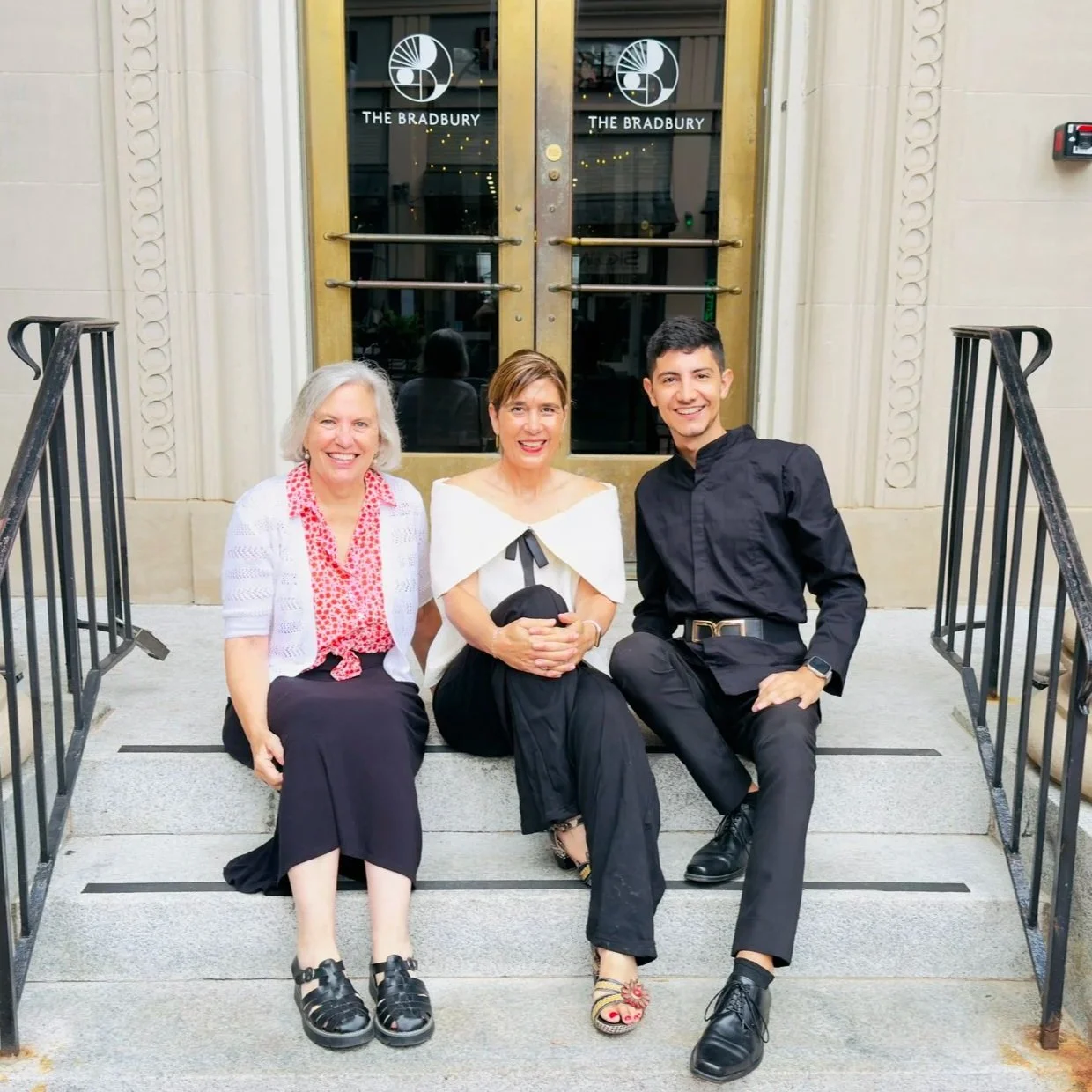 Three people sitting on the steps outside The Bradbury.