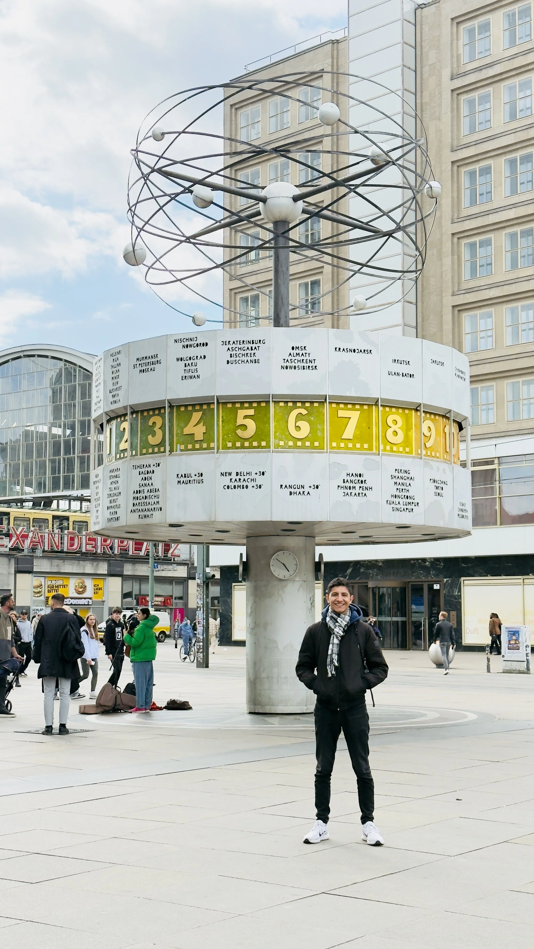 A man standing near a large world clock in a city square.
