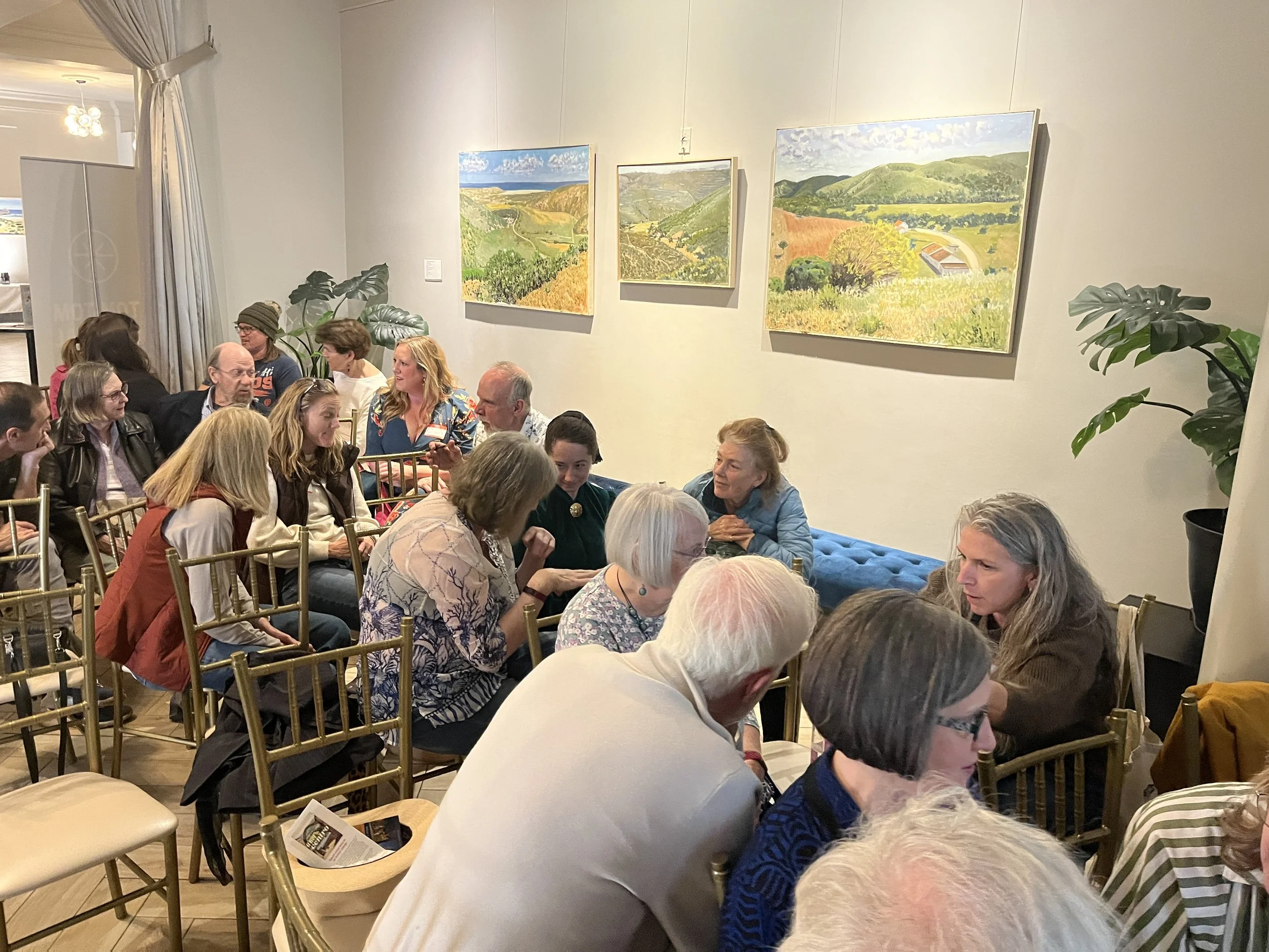 People sharing conversation in a room with landscape paintings.
