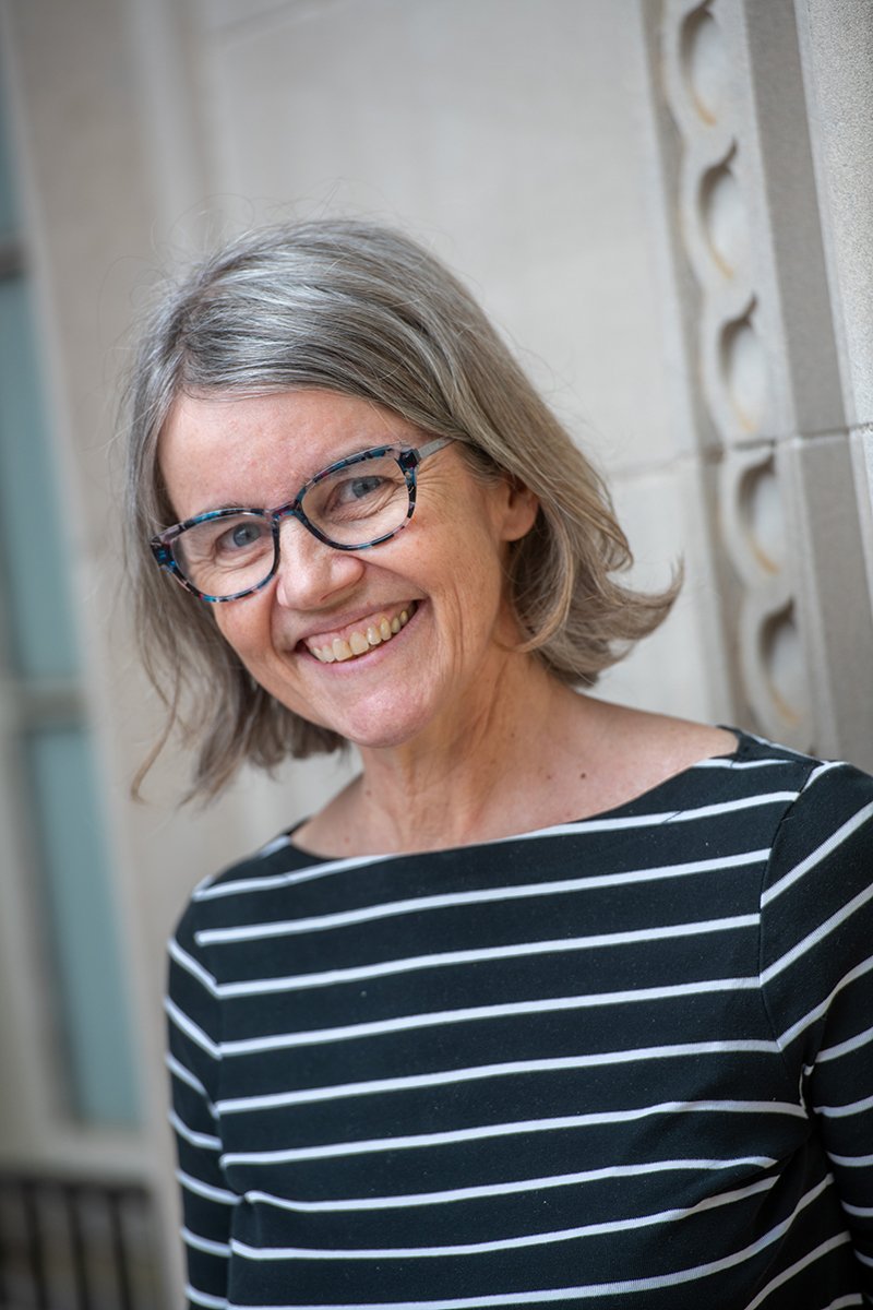 A smiling woman with glasses beside a stone building.