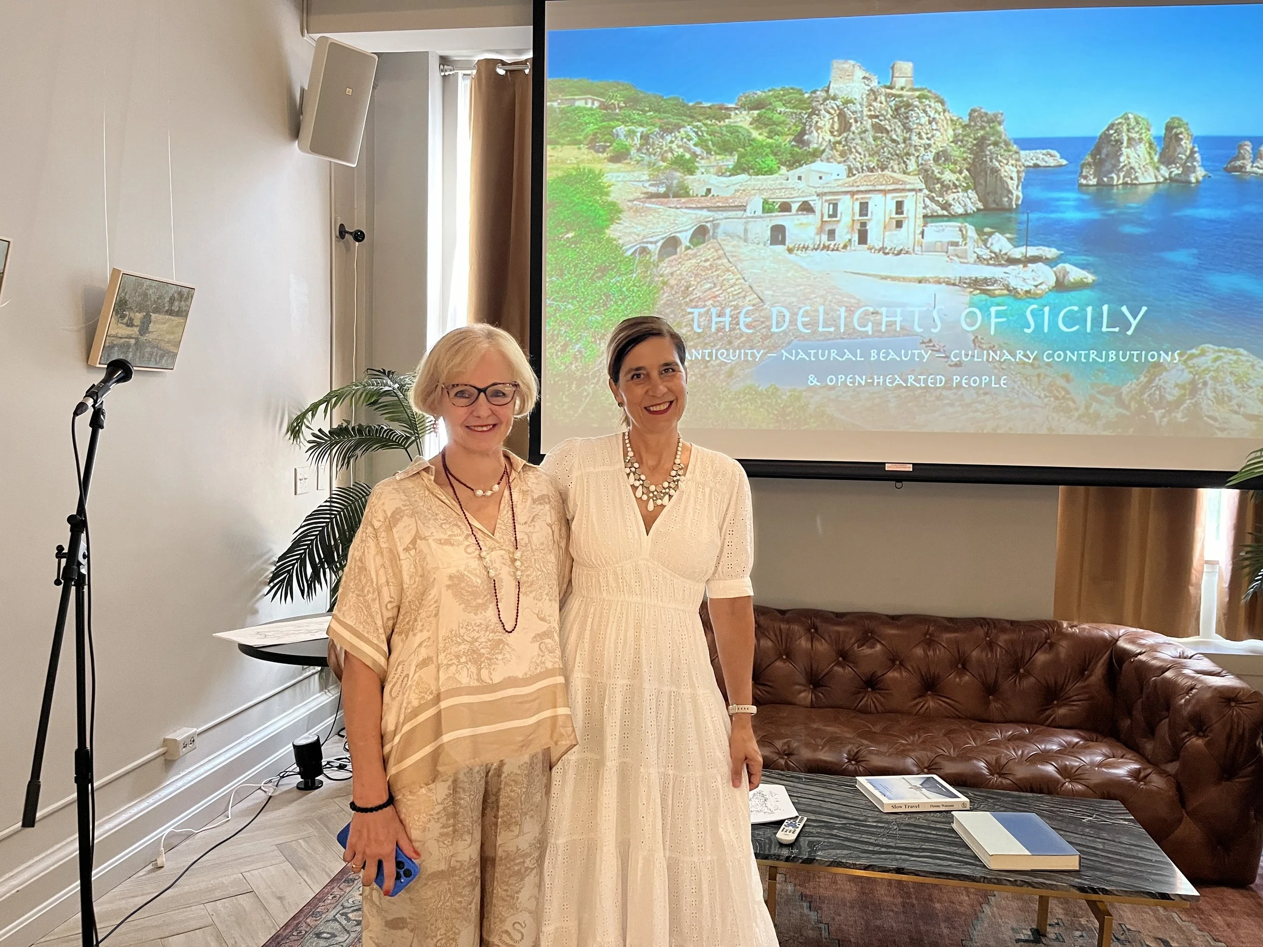 Two women beside a screen showing a Sicily presentation.