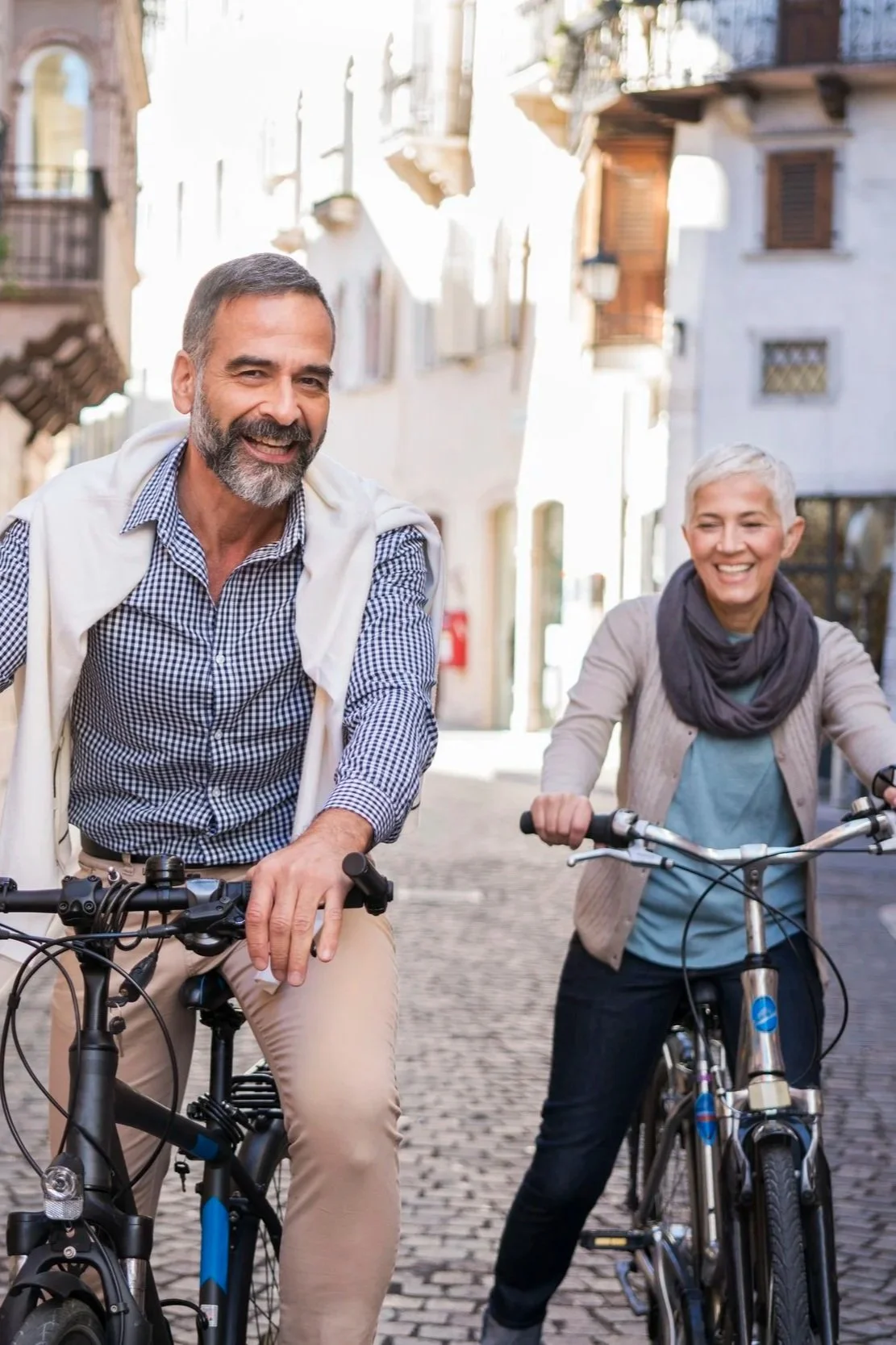 Two people smiling while riding bicycles along a city street.