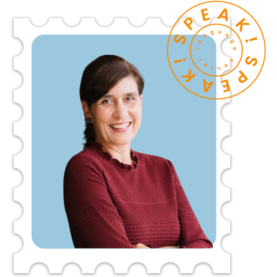 A woman with short dark hair and a maroon textured top smiling with her arms crossed against a light blue background, framed to look like a postage stamp.