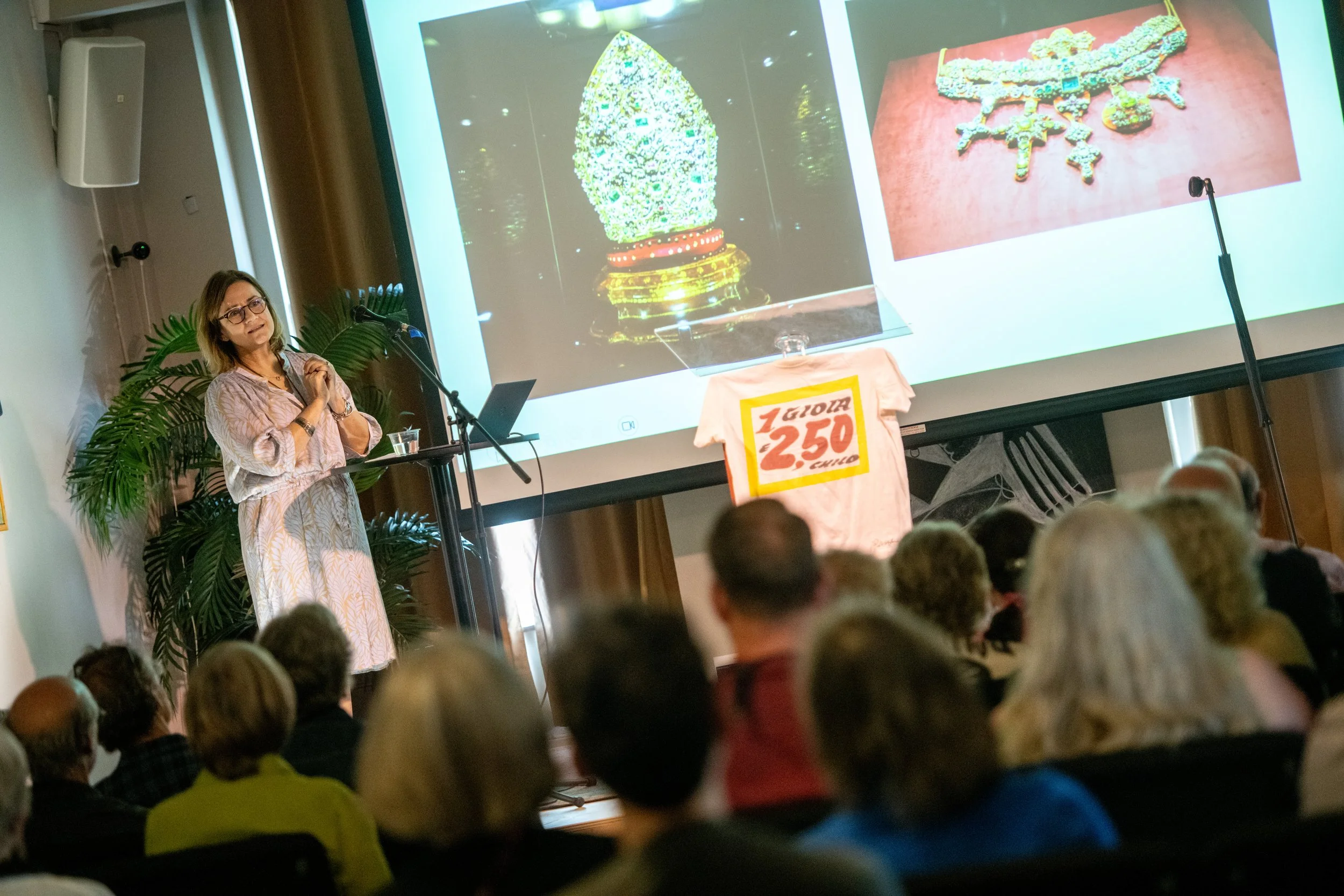 A woman presenting images of jewelry to an audience.