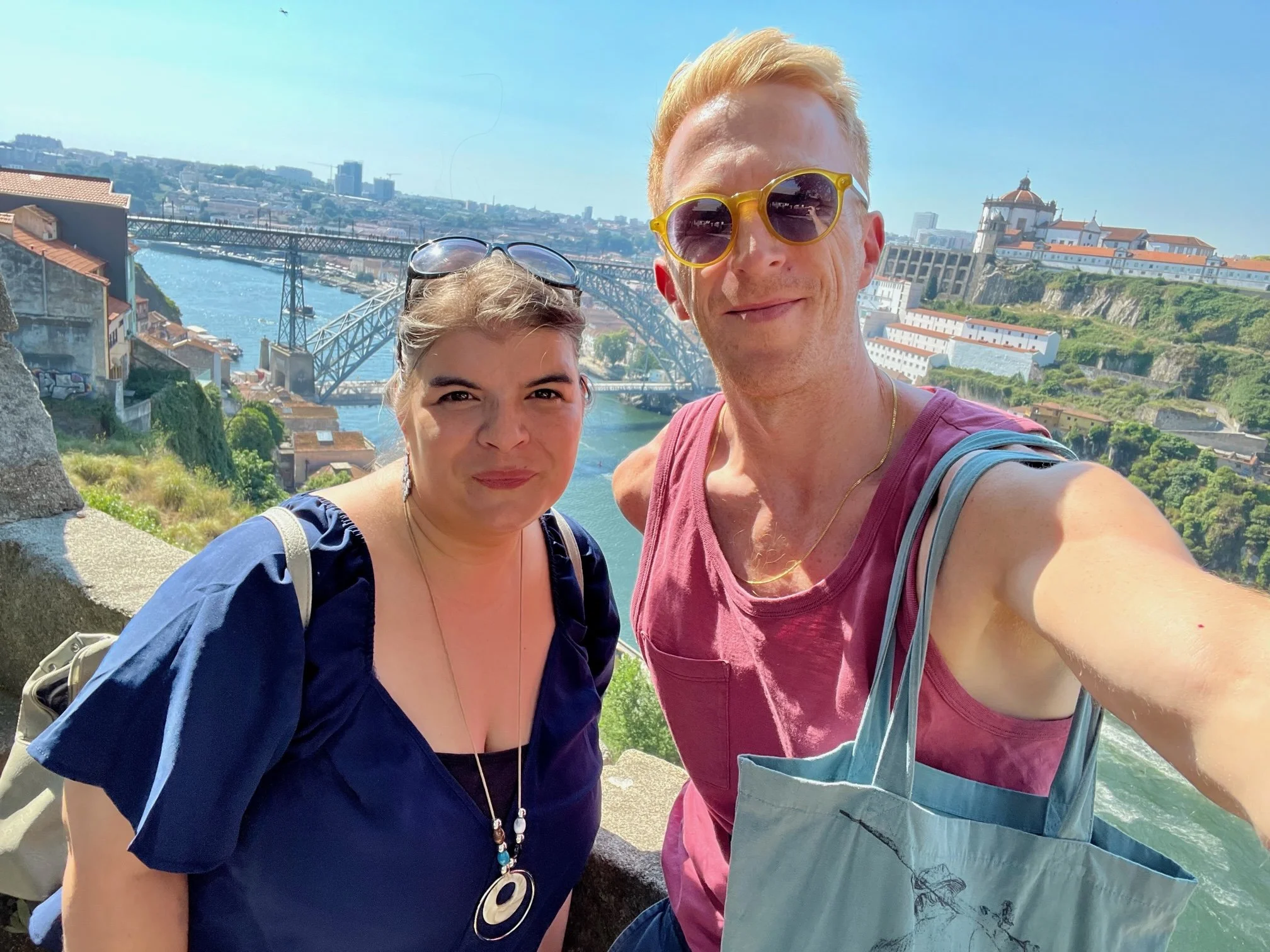 Two people taking a selfie above a river and cityscape.