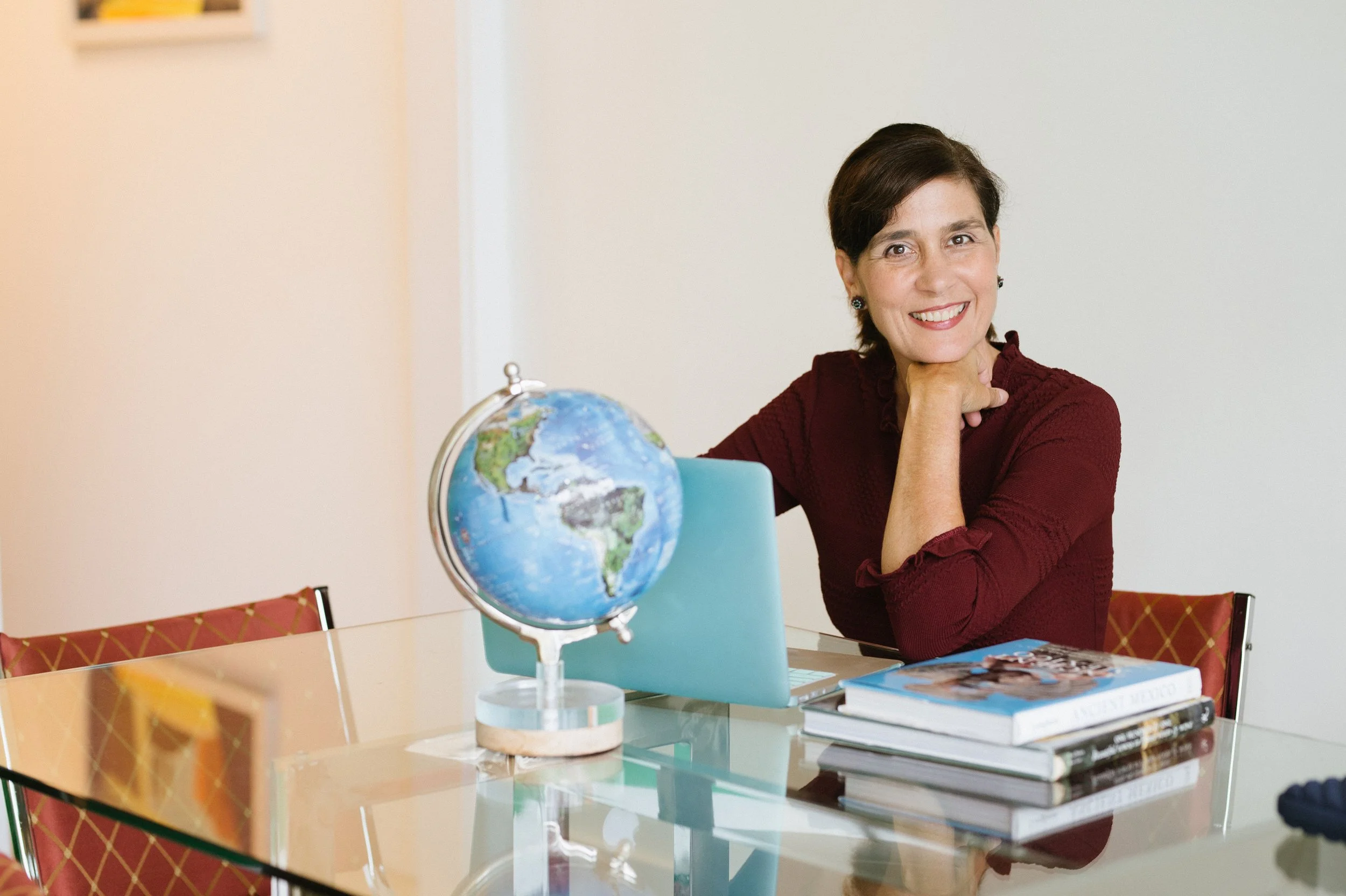A smiling woman at a desk with a globe and books.