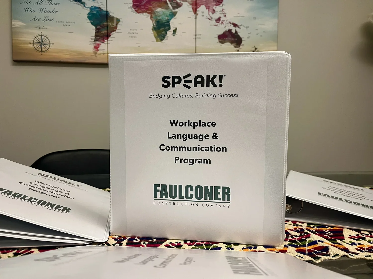 Workplace Language & Communication Program booklet on table with brochures, a map of world in the background.