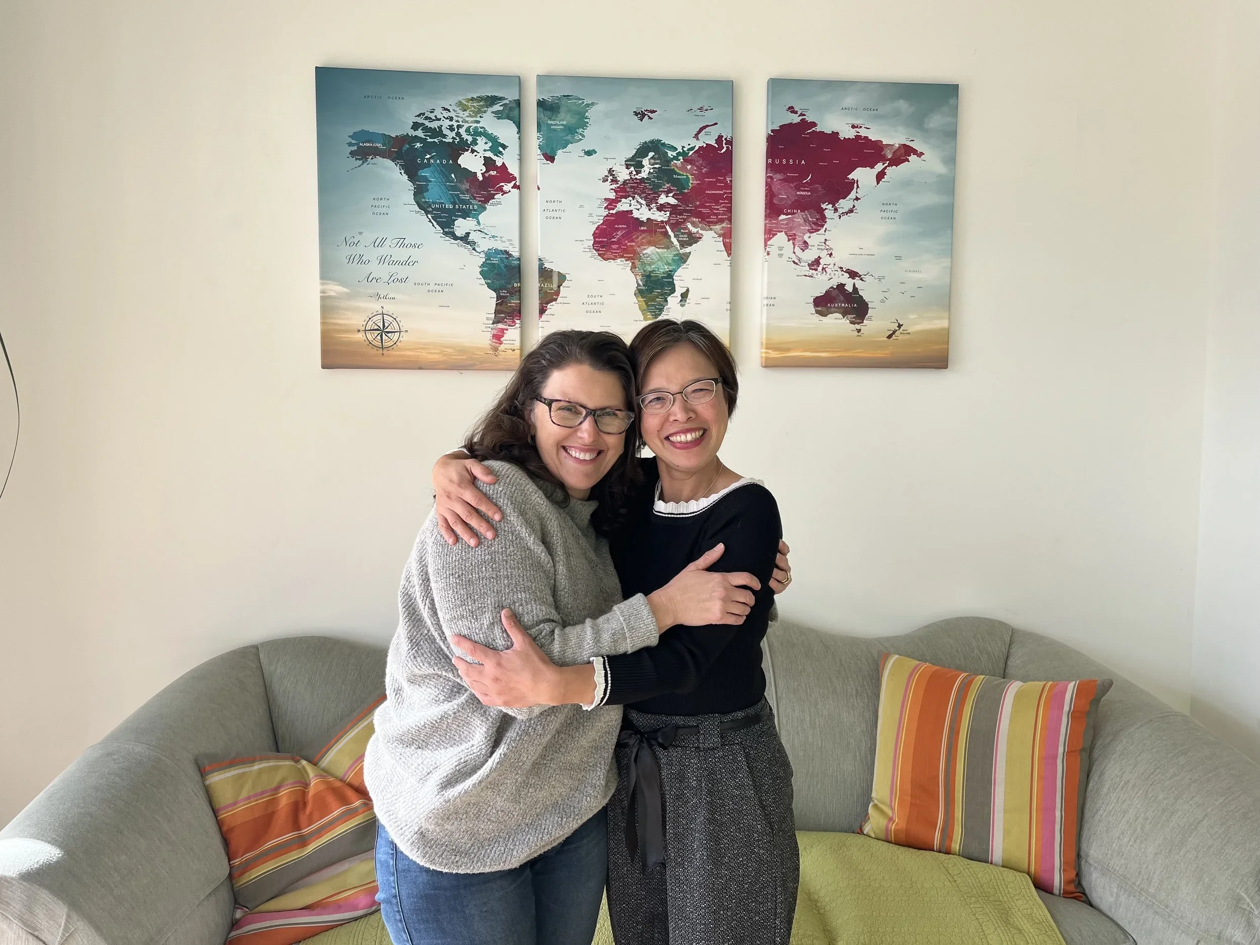 Two women smiling and embracing beside a world map.