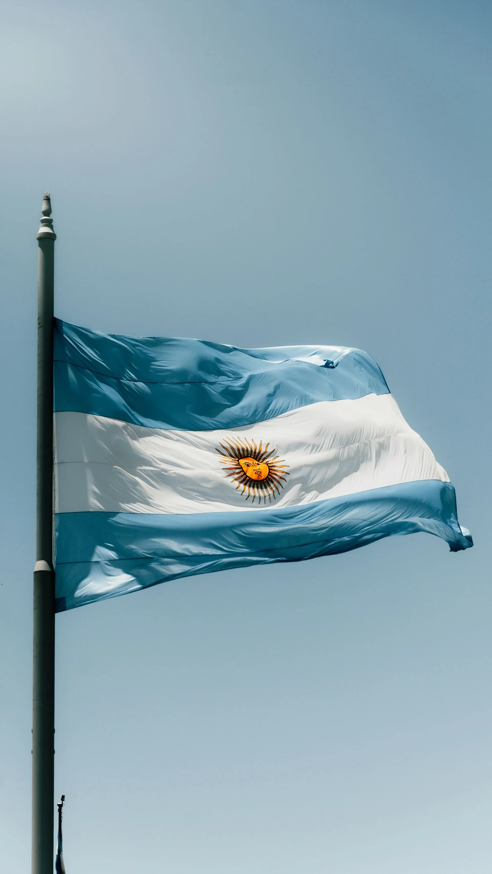 The national flag of Argentina, featuring three horizontal bands of light blue, white, and light blue, with a yellow sun with a face in the center of the white band.