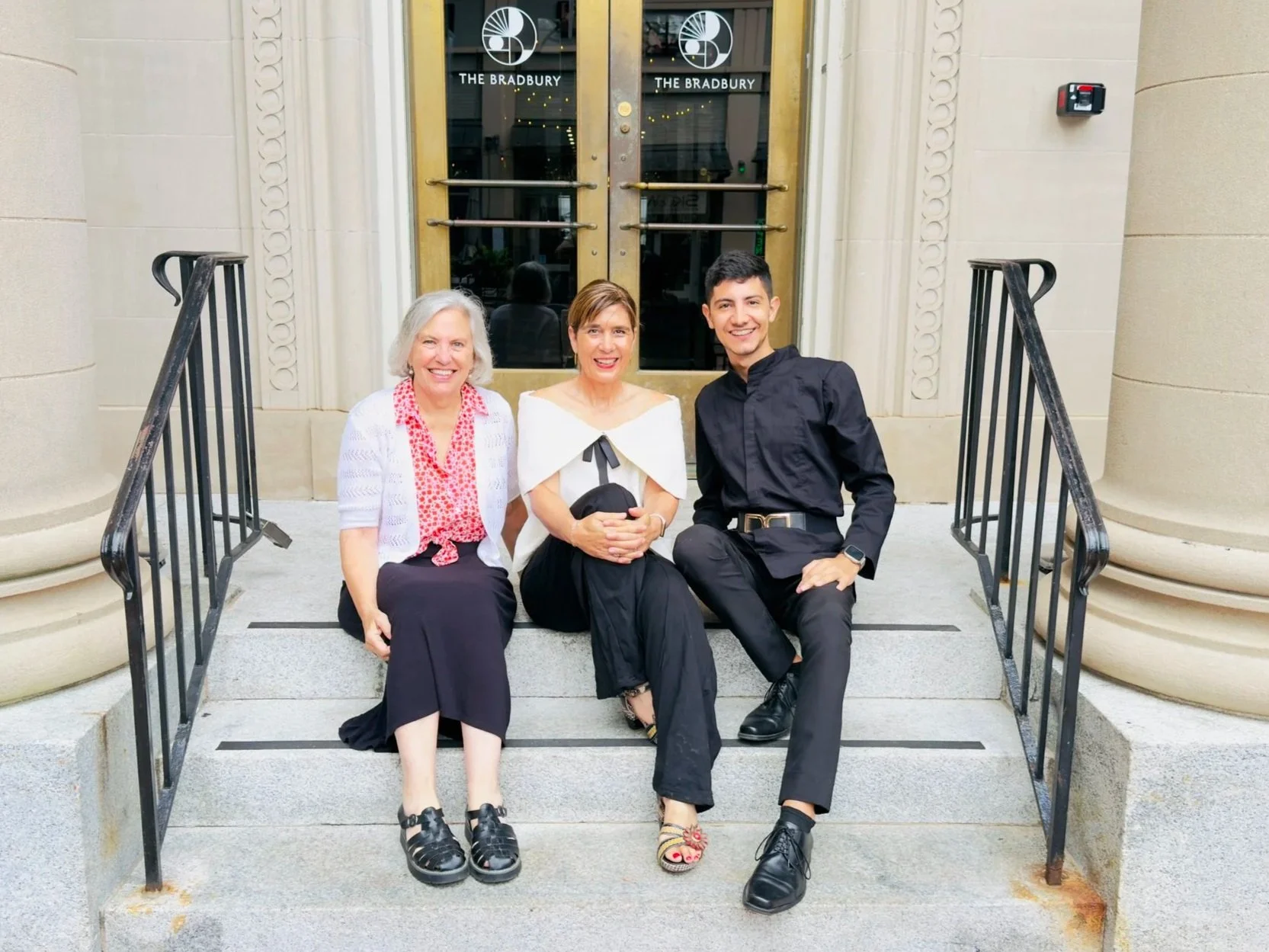Three people seated on steps outside a building.