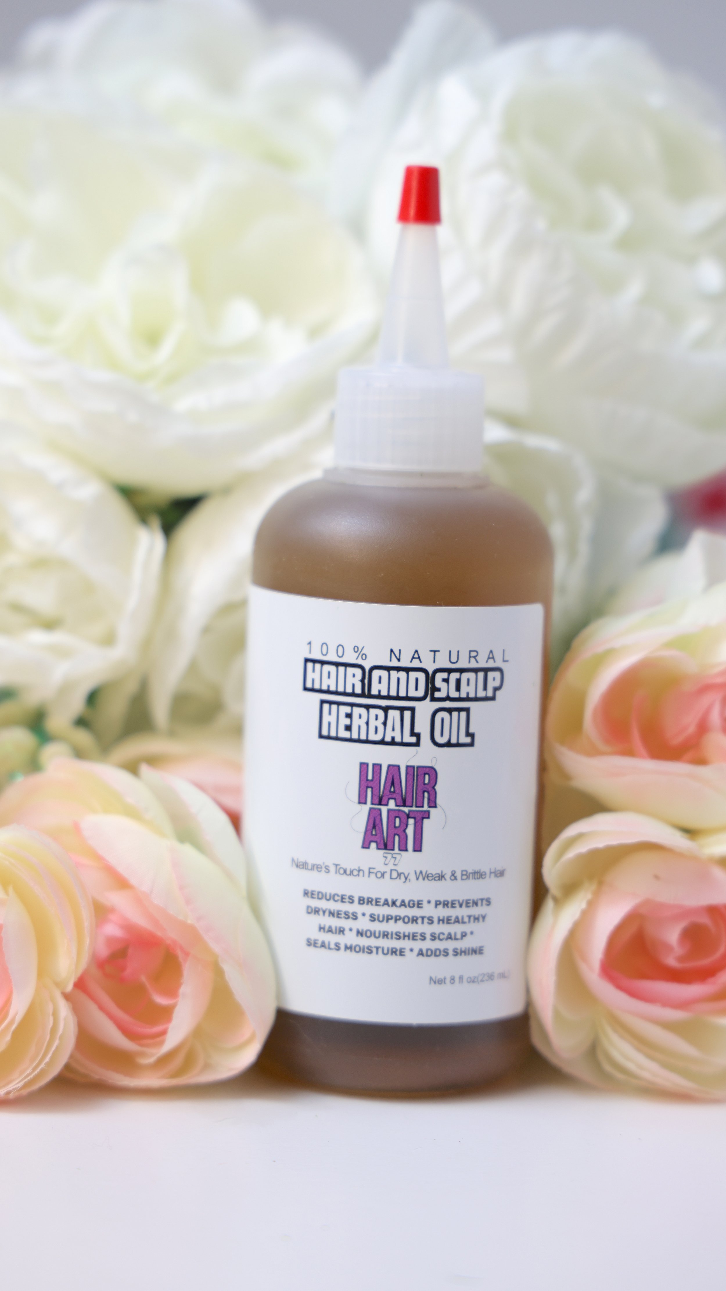 Bottle of hair and scalp herbal oil labeled 'Hair Art' surrounded by white and pink roses.