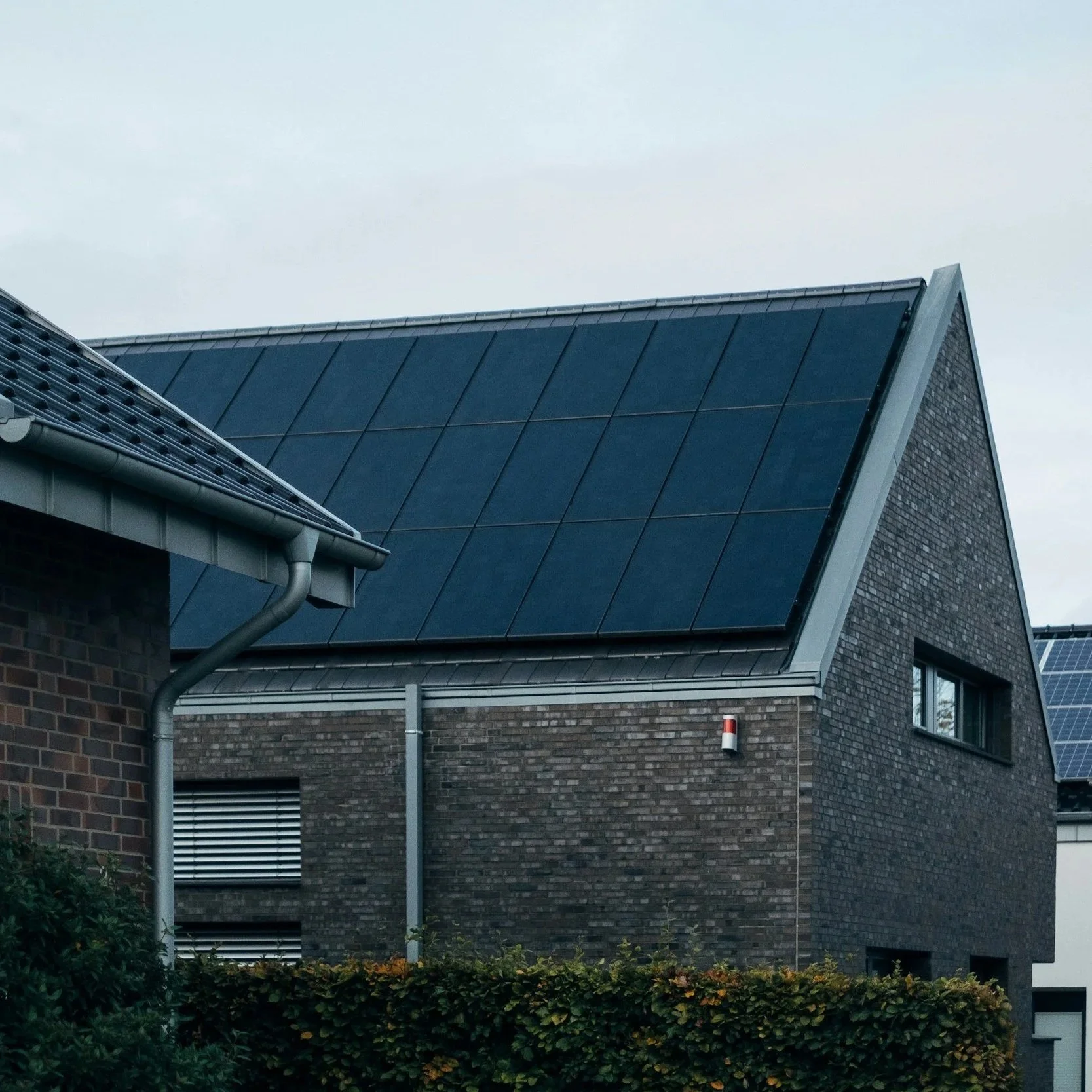 A modern house with a dark brick exterior and a steeply pitched roof covered in solar panels.