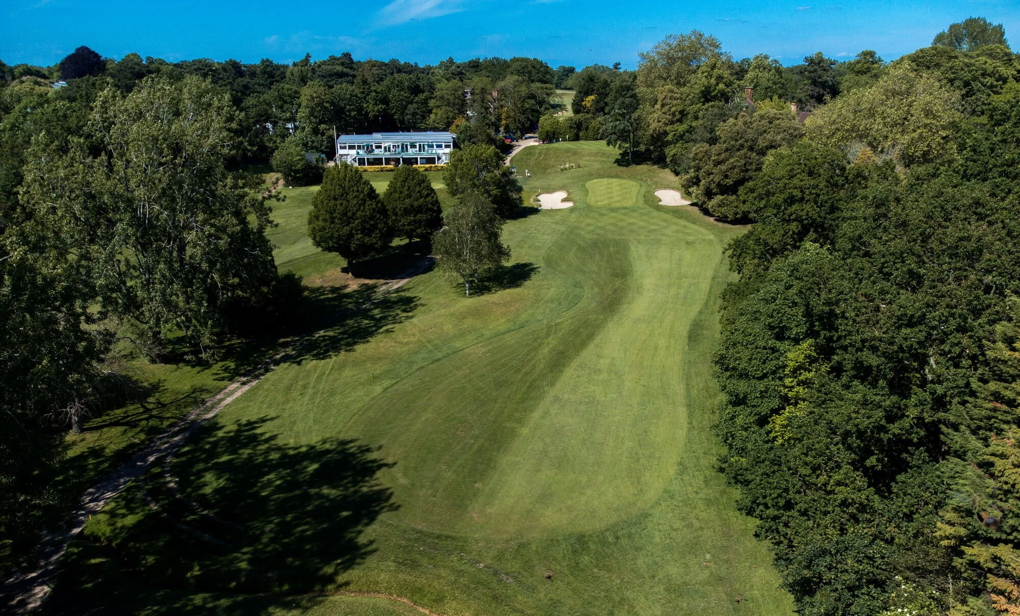 Aerial view of a golf course surrounded by trees, with a building in the background and sand bunkers near the green.