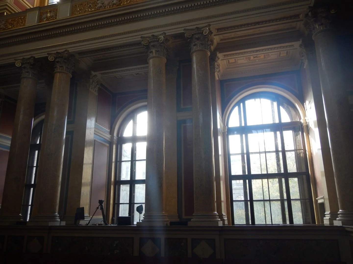 Innenraum mit hohen Fenstern, großen Säulen und kunstvoller Decke, wahrscheinlich ein historisches Gebäude oder Palast.