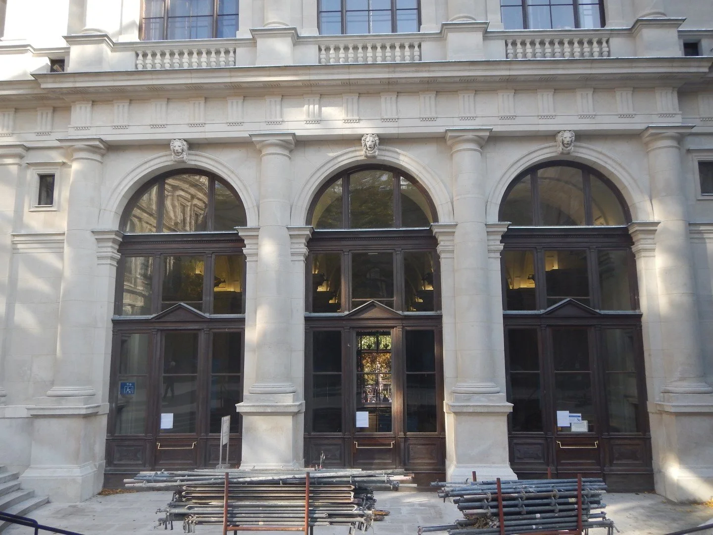 Fassade eines Gebäudes mit großen bogenförmigen Fenstern und kunstvollen Verzierungen, Bauarbeiten vor dem Eingang.
