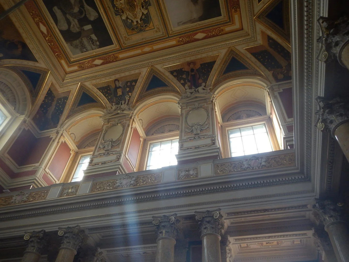 Dekorative, barocke Innenarchitektur mit hohen Fenstern, goldverzierten Kolonnen, aufwendigen Verzierungen, Wandbildern und einem tiefblauen Himmelmotiv auf der Decke.