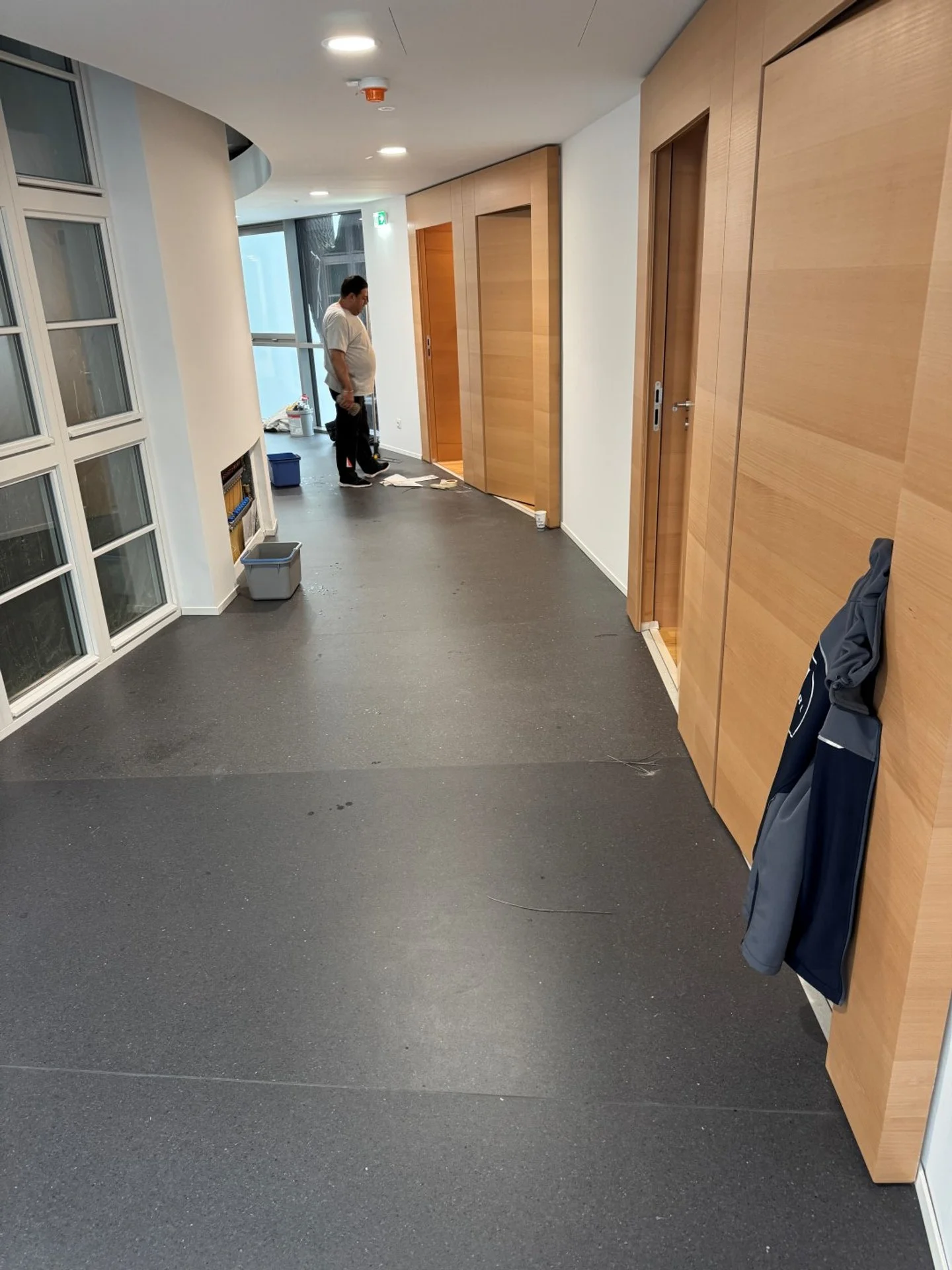 Innenaufnahme eines Flurs mit Holzschiebetüren, ein Mann steht vor einer Tür, es gibt Umzugskartons und Reinigungsutensilien am Ende des Flurs.