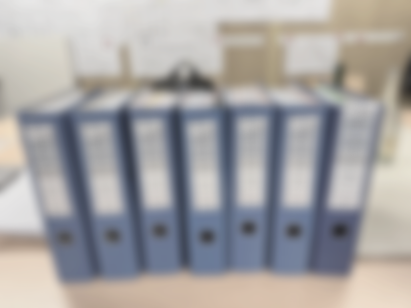 Mehrere blaue Aktenordner nebeneinander auf einem Schreibtisch.